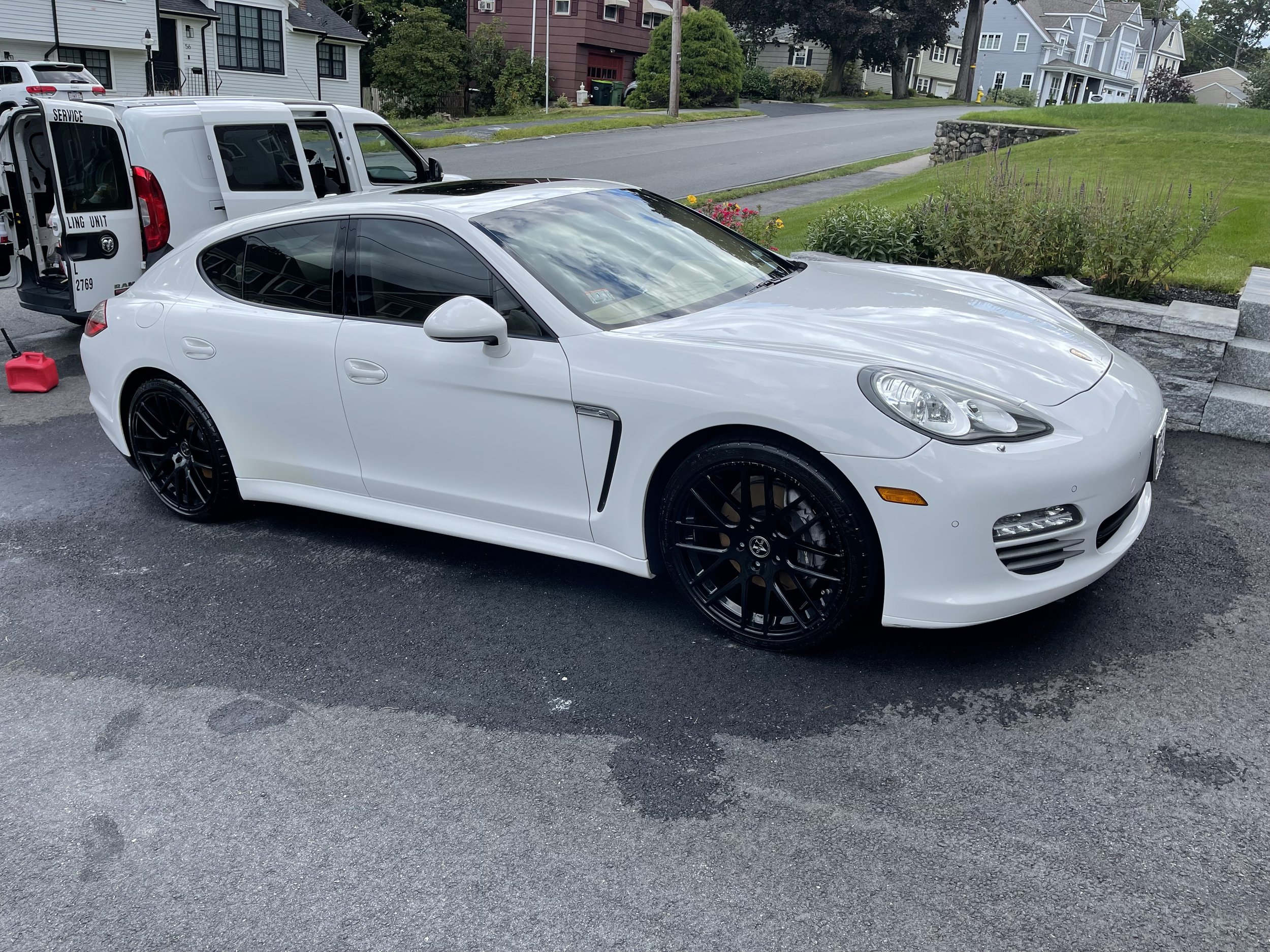 White sports car parked on a driveway with a service van nearby