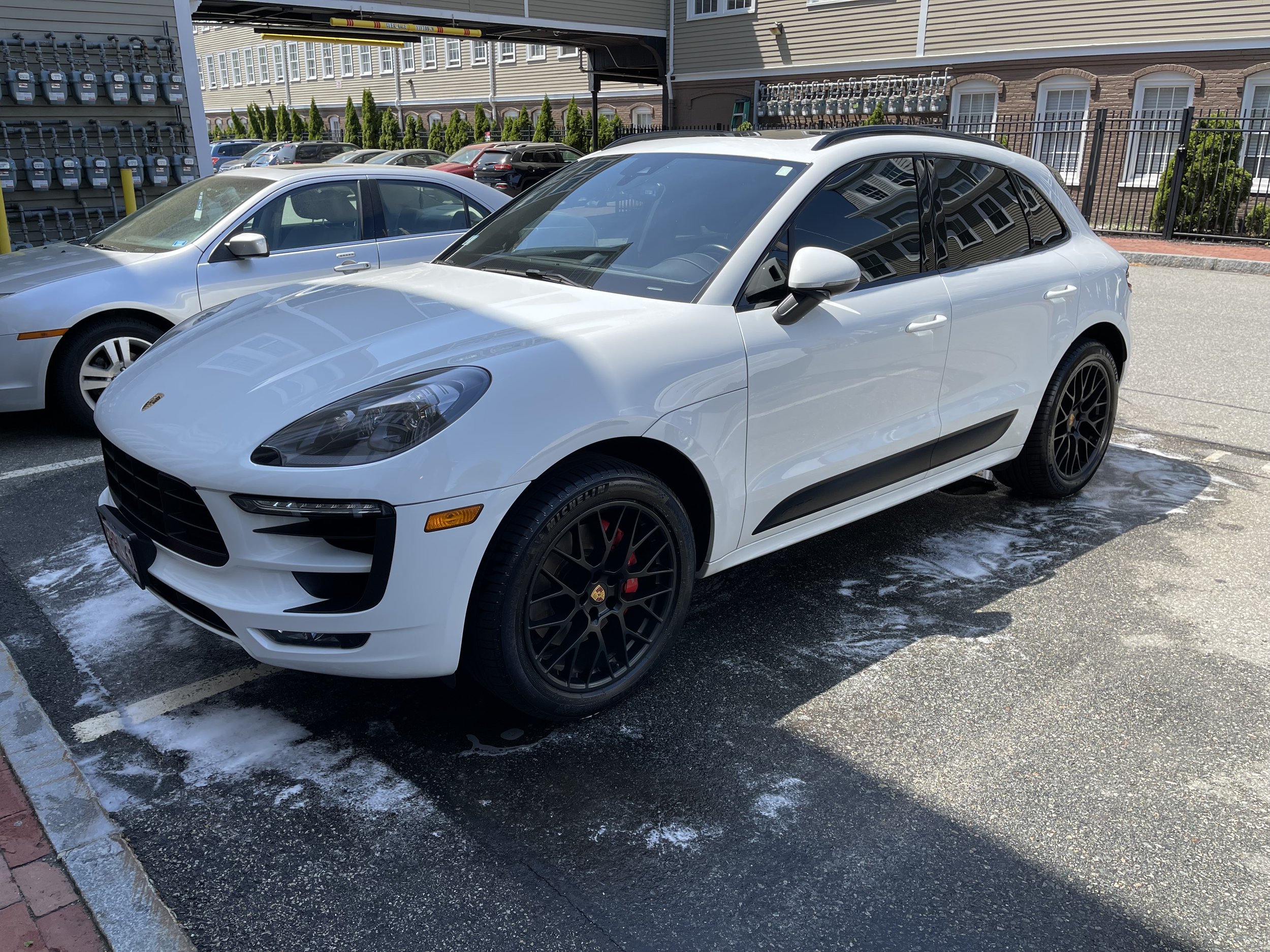 White Porsche SUV parked beside a silver sedan in a parking lot.