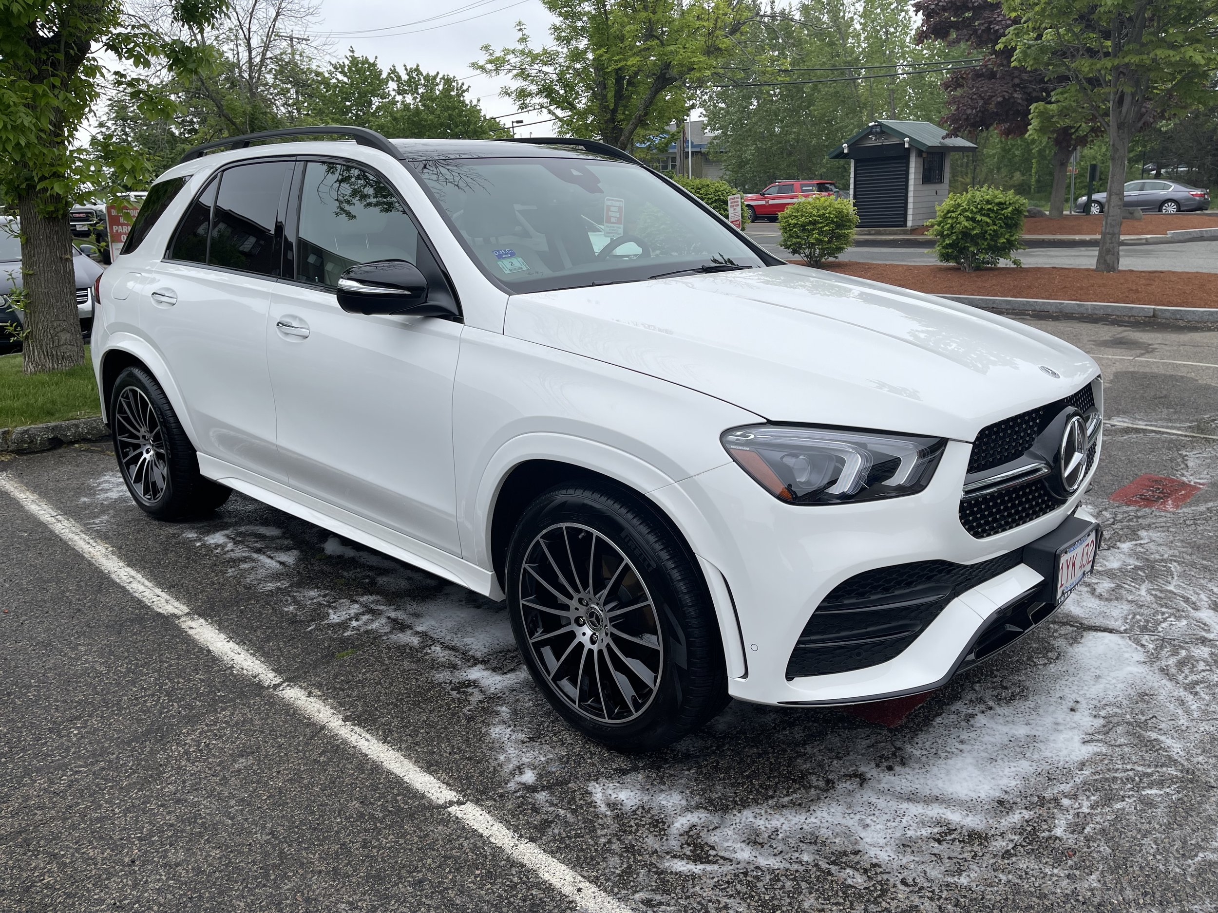 White Mercedes-Benz SUV parked in a parking lot, surrounded by trees.