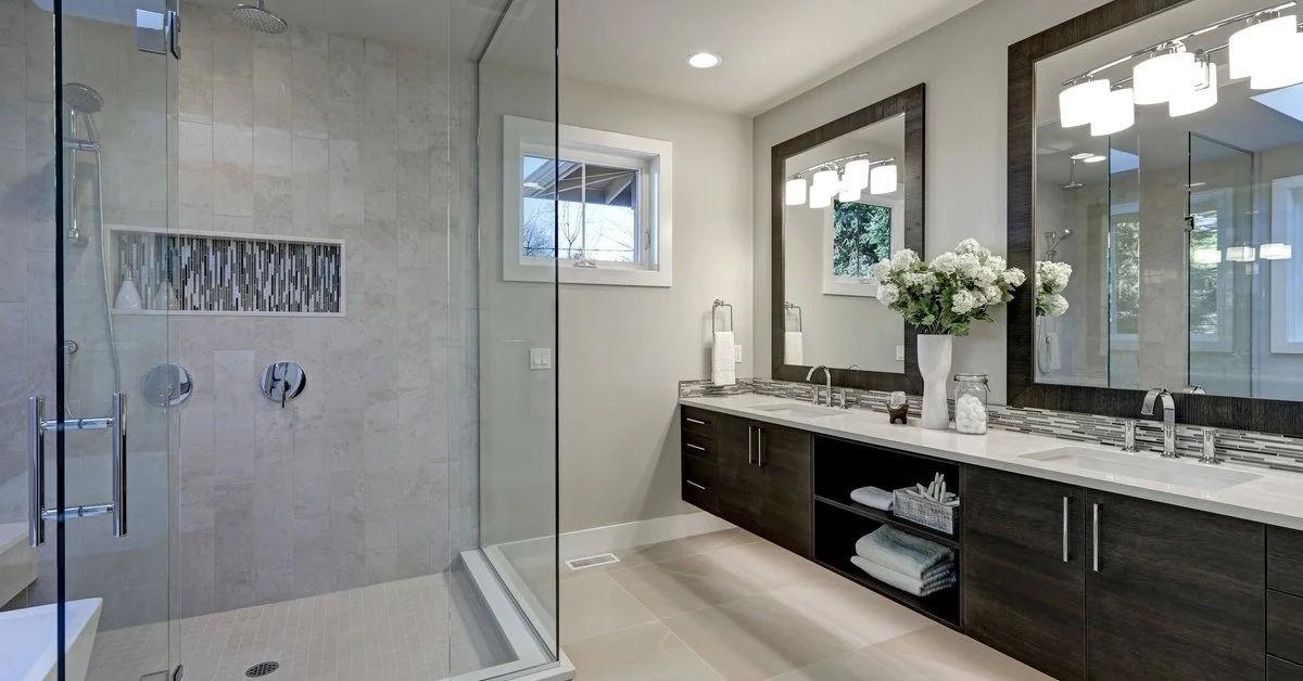A wide shot of a bathroom with a frameless shower, a double sink vanity, and two separate, framed mirrors.