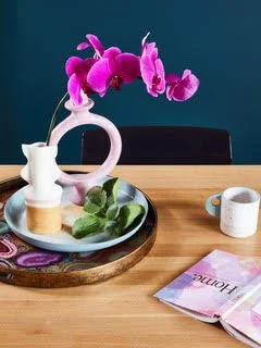 Beautifully styled dining table with a hot pink orchid in a sculptural pink vase, white jug, and curated tray against a deep teal feature wall — interior styling inspiration by The Home Studio Co