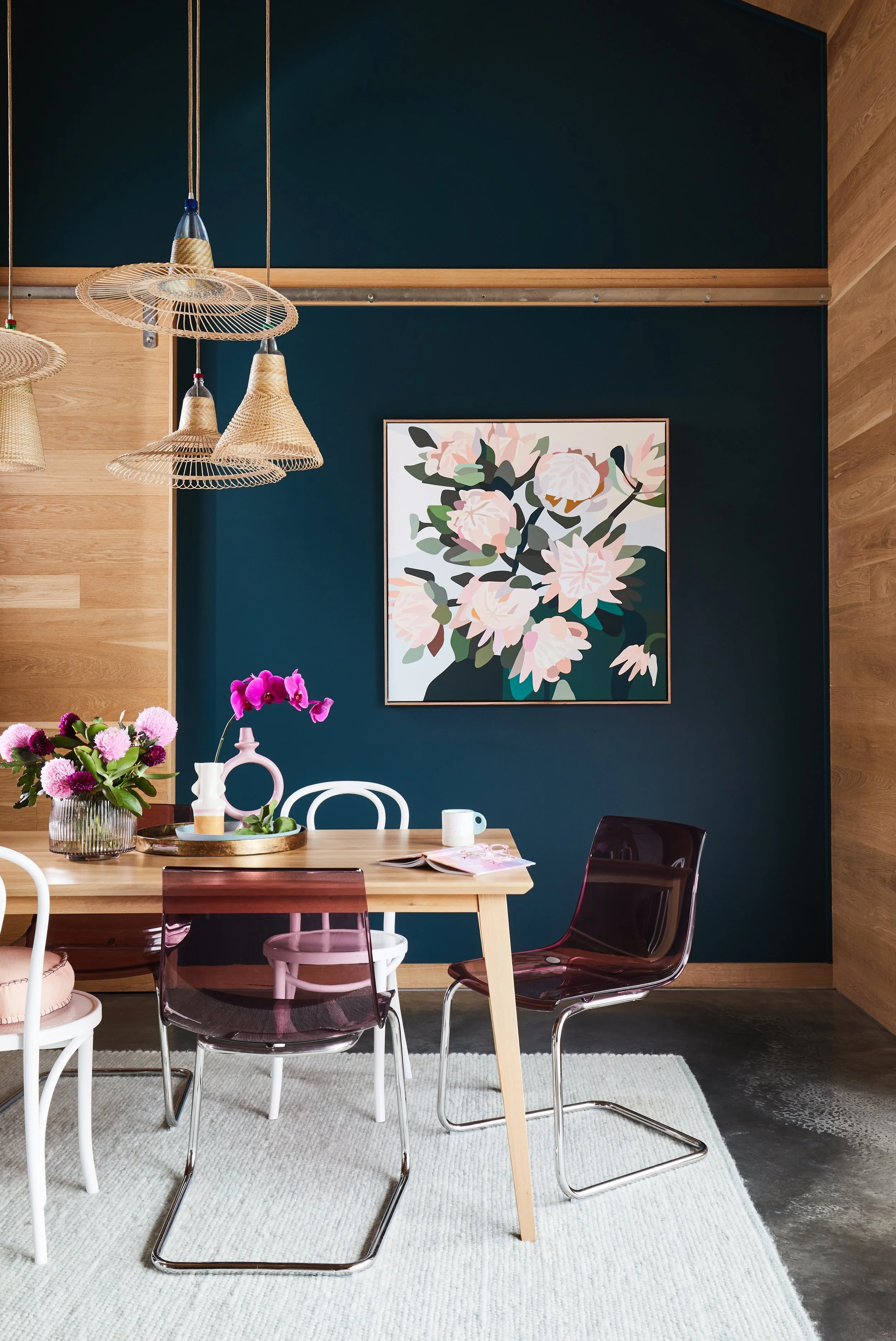 Styled dining with with deep teal feature wall, large floral canvas artwork, mixed chair styles including bentwood and acrylic, rattan pendant lights, fresh flowers on a timber dining table. Bold interior styling inspiration from The Home Studio Co