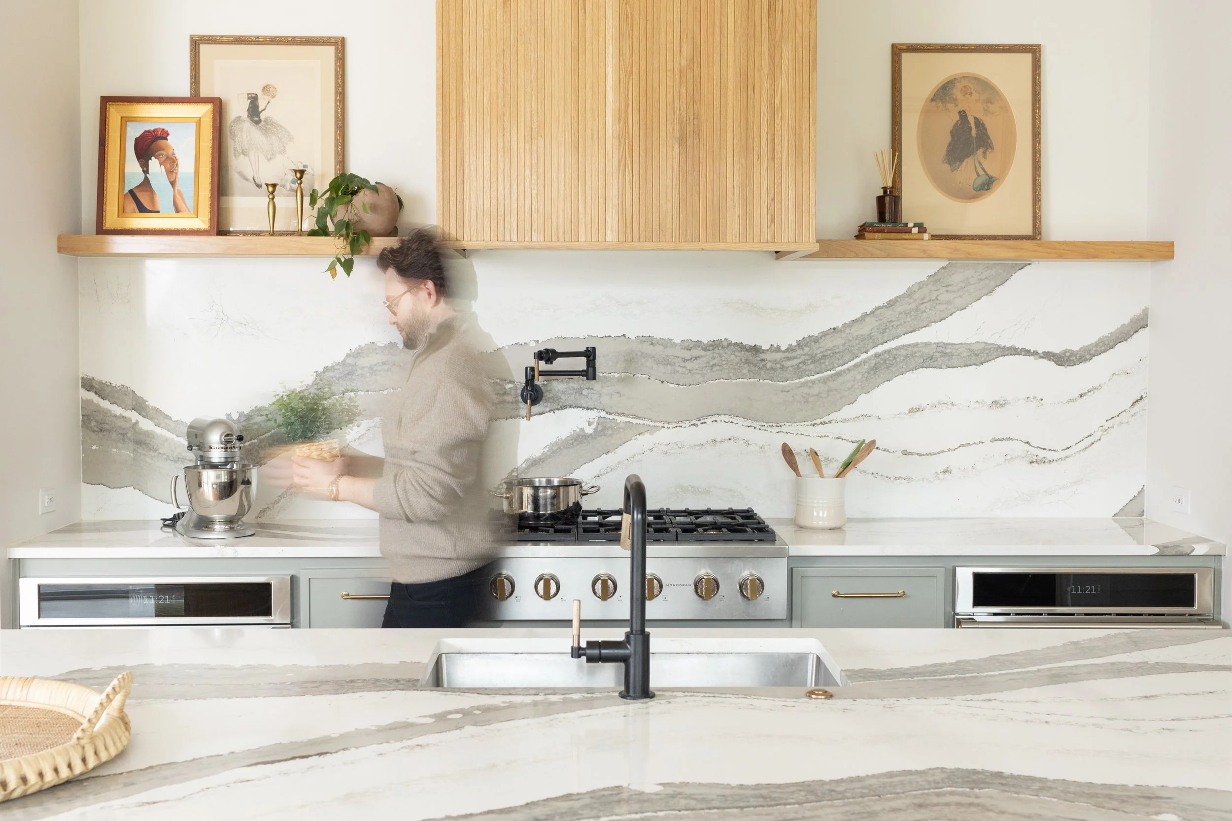 Modern kitchen in Fort Worth, Texas with marble countertops, a man standing by a KitchenAid mixer, artwork on the shelf, and a stove with a pot. The backsplash and counters have a gray, wavy pattern.