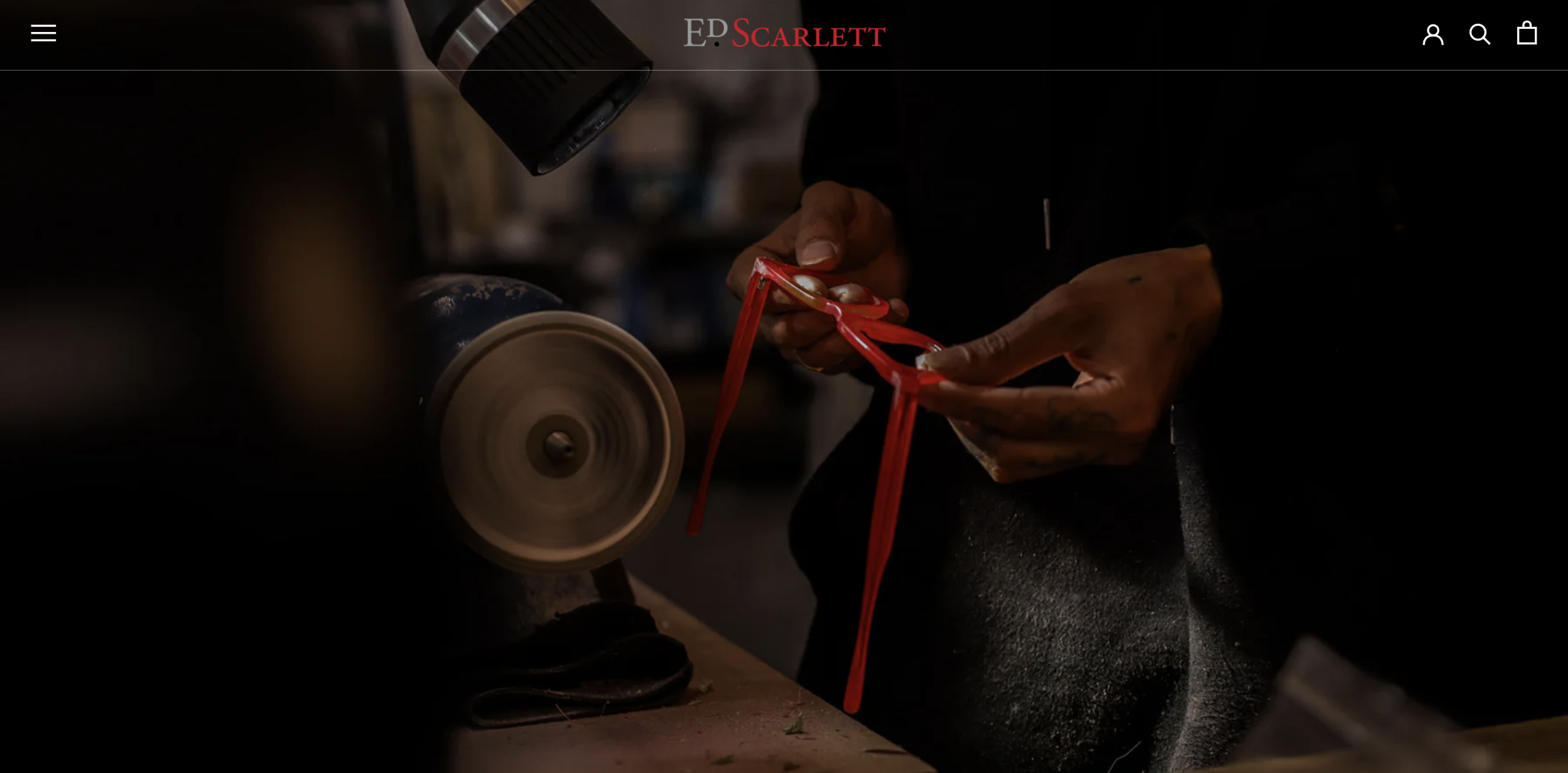 A person polishing red sunglasses with a polishing wheel in a workshop.
