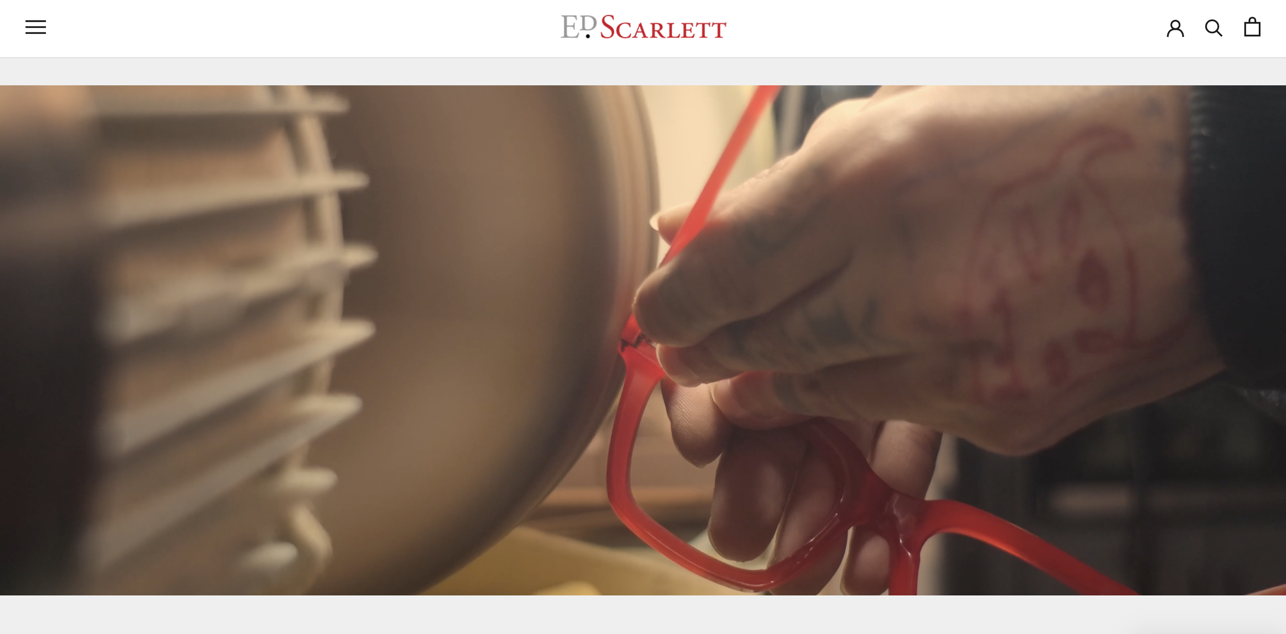 Close-up of a tattooed hand holding red eyeglasses near a metallic object with horizontal slats.