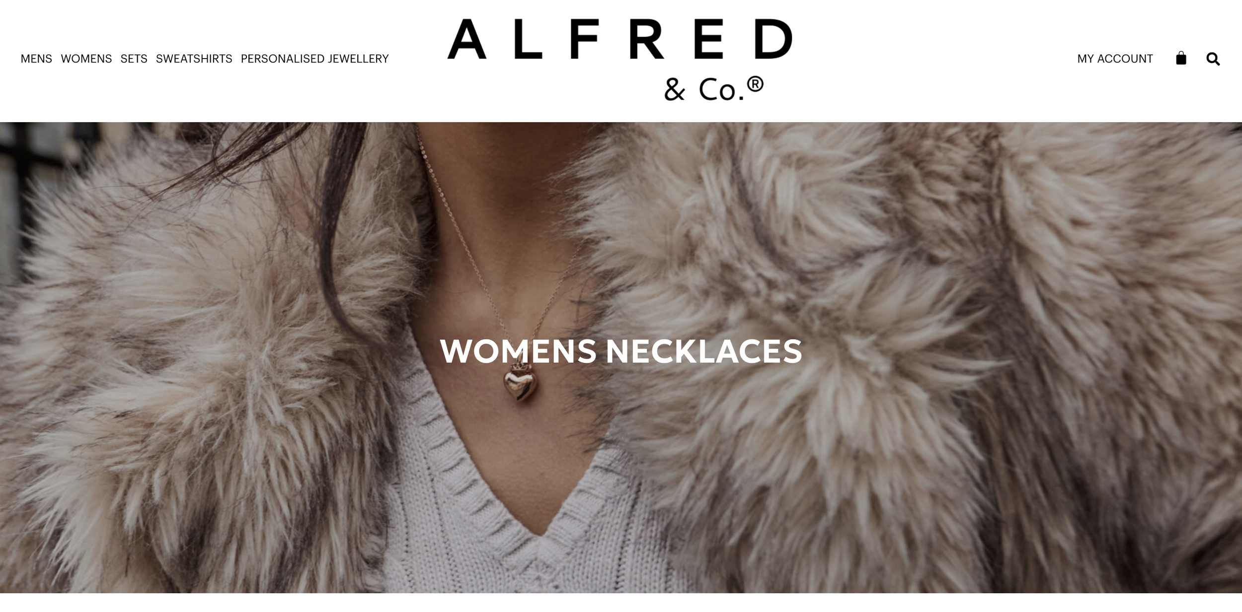 Close-up of a woman's neck wearing a heart-shaped necklace, with a faux fur coat and a light-colored sweater.