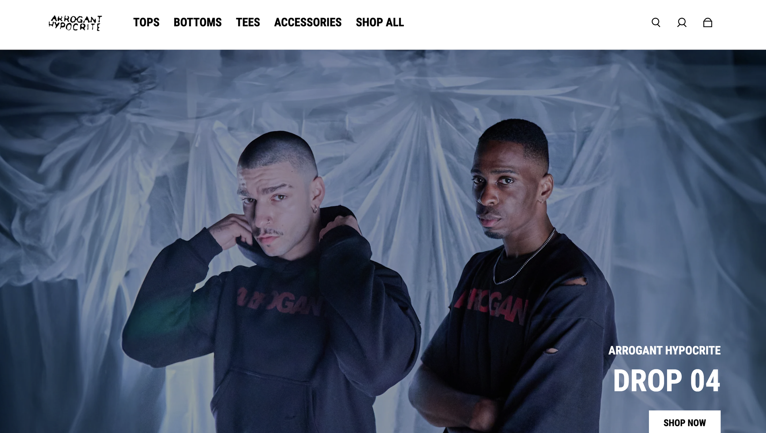 Two young men stand in front of a translucent plastic backdrop. They are wearing black hoodies with red lettering and have serious expressions. The scene has a moody, urban aesthetic.