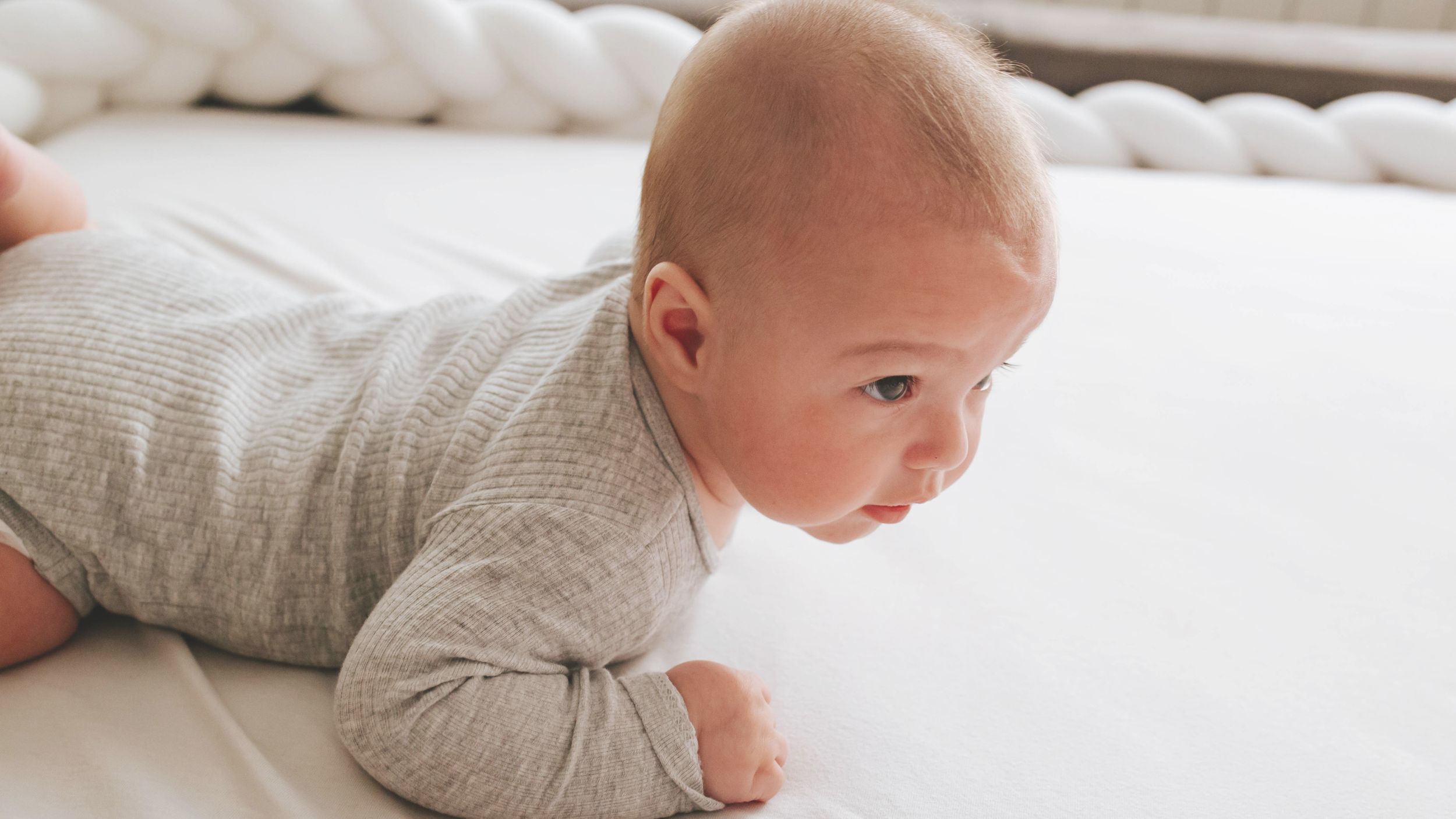Young child crawling on a bed with a white mattress and white bedding.