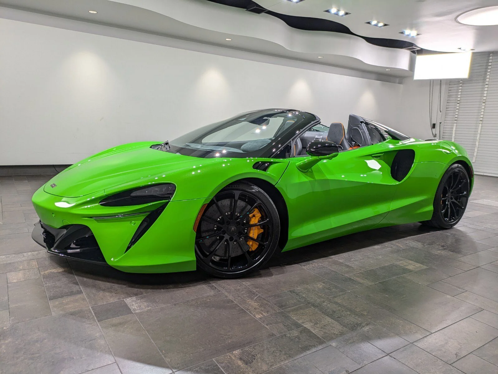 A bright green luxury convertible sports car parked indoors against a white wall.