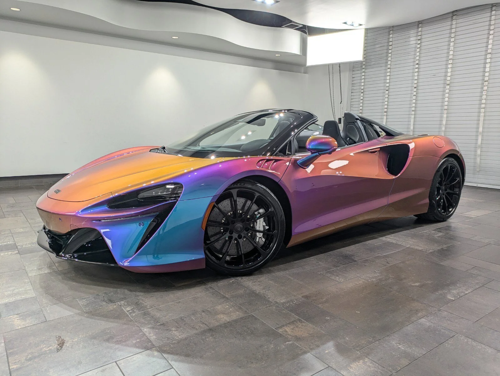 A colorful, iridescent convertible sports car with black wheels parked indoors.