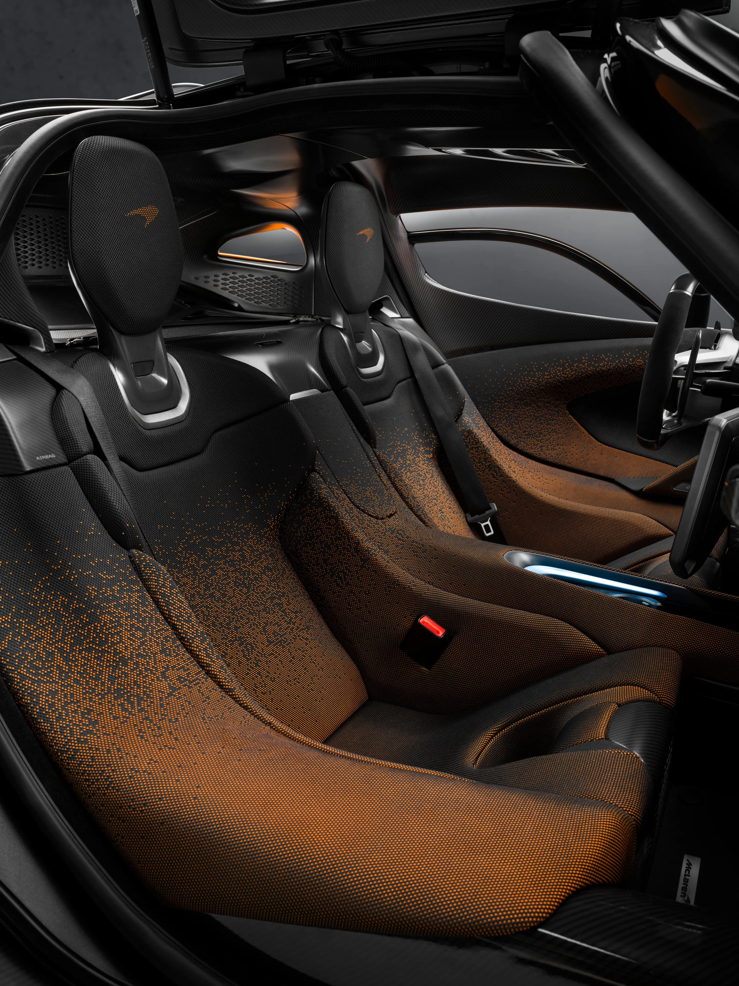 Inside view of a high-tech sports car interior with black and orange seats, headrests featuring a small logo, and a modern dashboard.