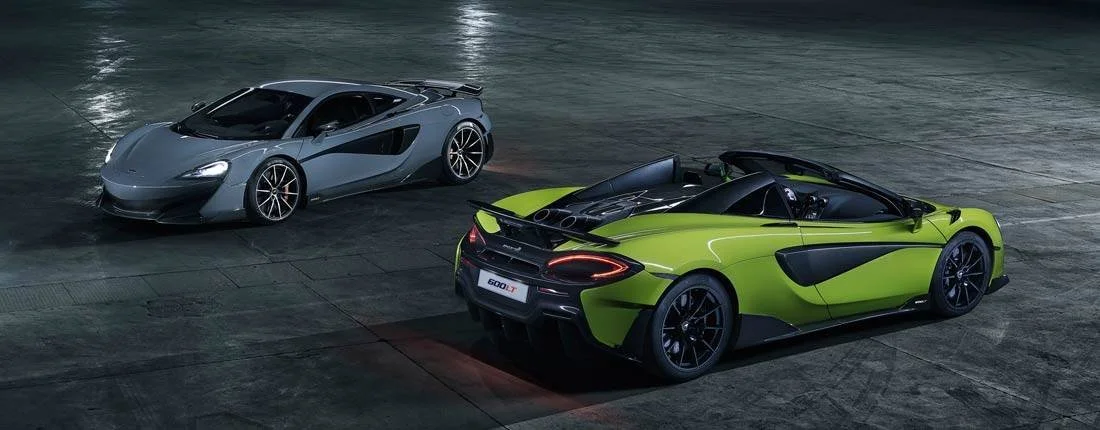 Two sports cars parked on an empty concrete surface at night, one silver and one bright green with black accents.