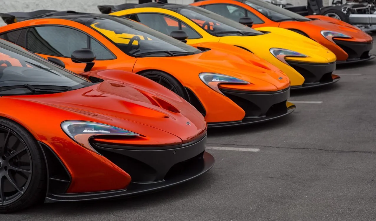 A row of colorful McLaren cars parked in a lot, featuring red, orange, yellow, and black models.