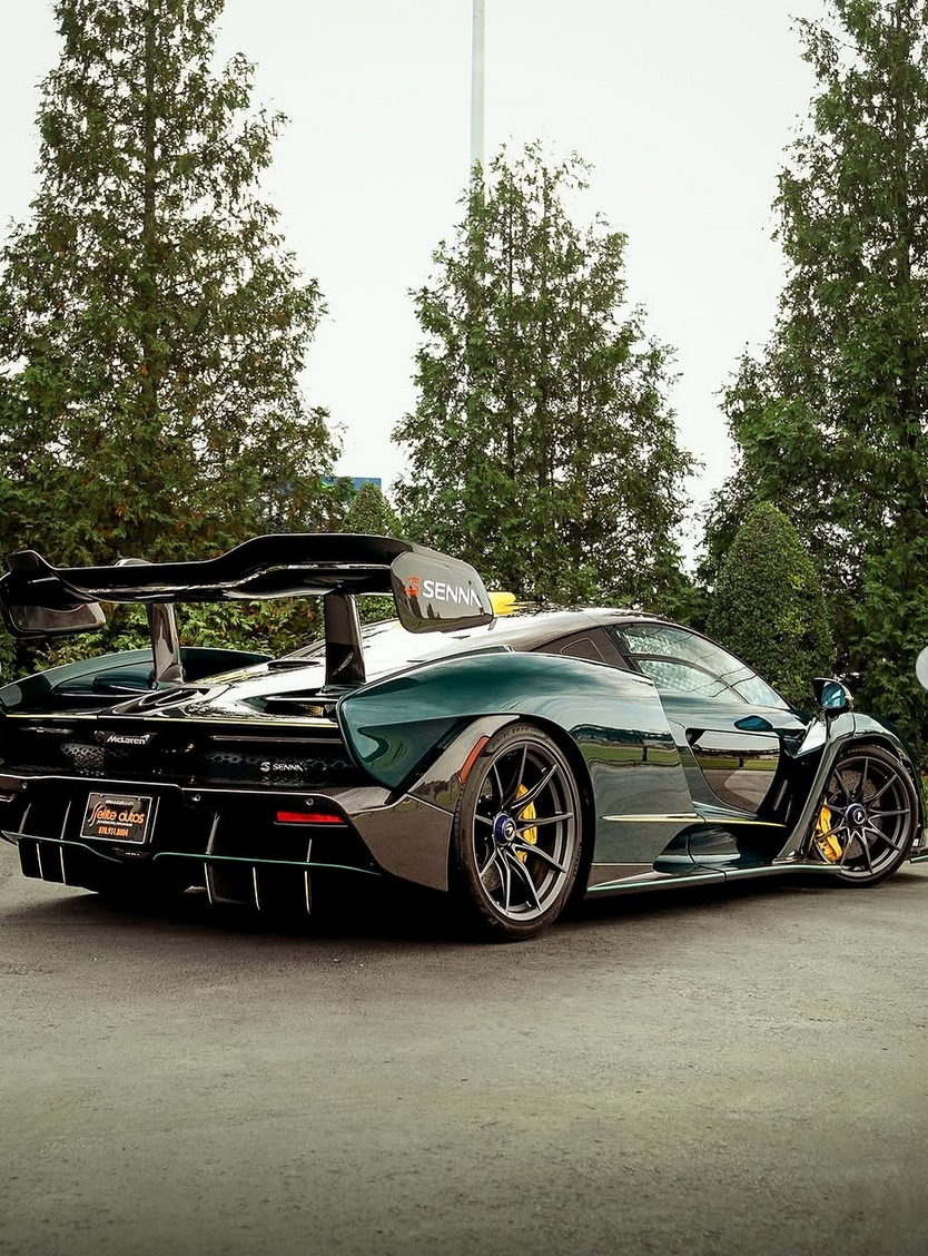 A black and green McLaren Senna supercar parked outdoors with trees in the background.
