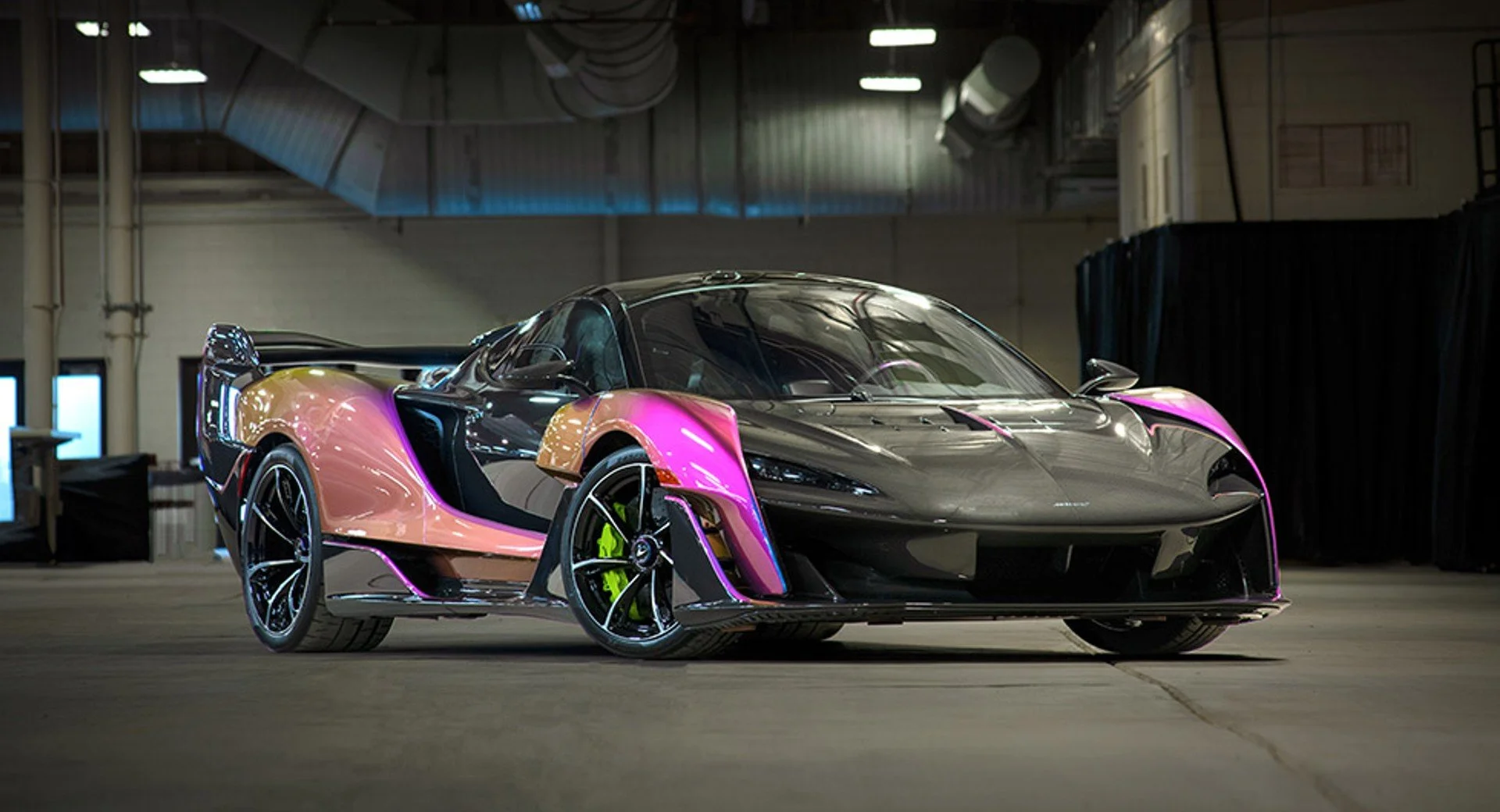 A sleek hypercar with a black and pink color scheme parked inside an industrial building.