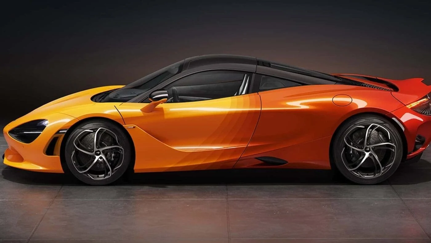 A sleek, orange and black luxury sports car displayed on a dark showroom floor, featuring modern aerodynamic design with black racing wheels and tinted windows.