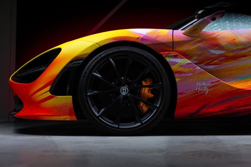 Close-up of a yellow and red sports car with colorful graphics, focusing on the front wheel and side panel.