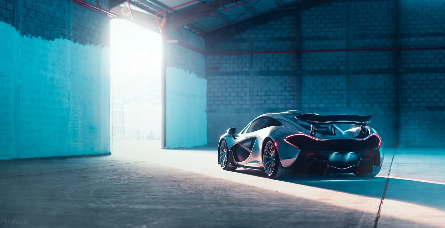A sleek, futuristic sports car parked inside a dimly lit garage with an open door revealing bright sunlight outside.