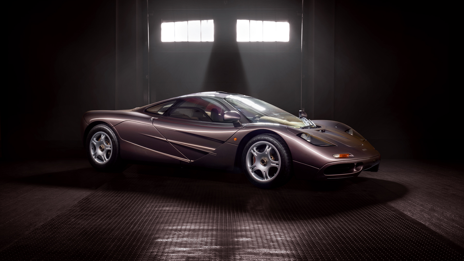A sleek, metallic purple sports car in a dimly lit garage with a large window providing backlighting.