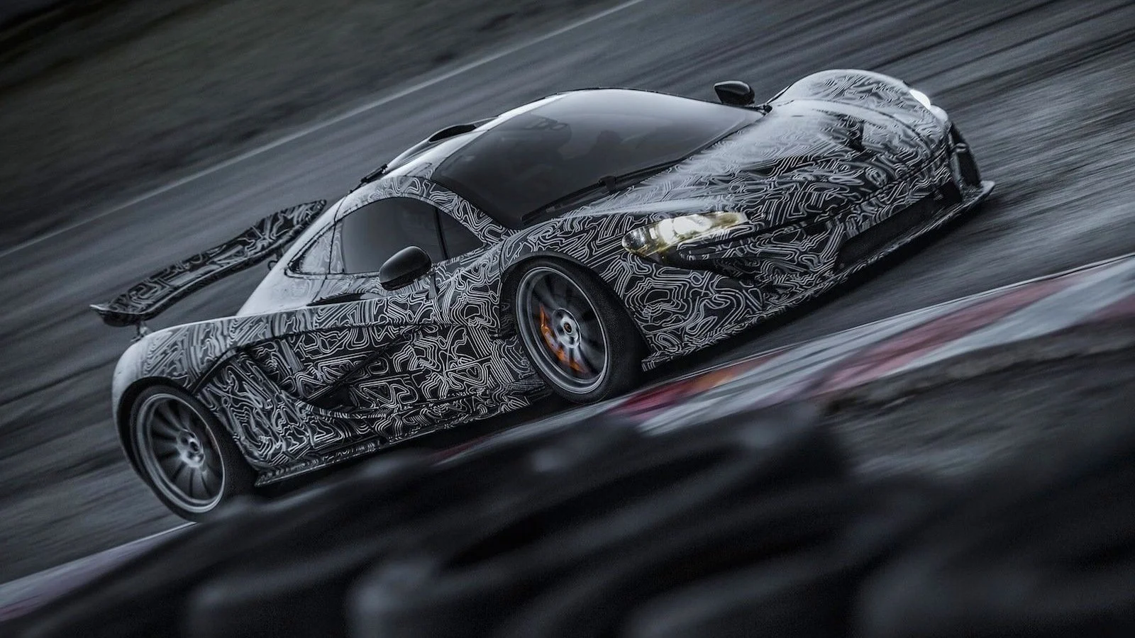 Test mule sports car with camouflage body panels racing on a track