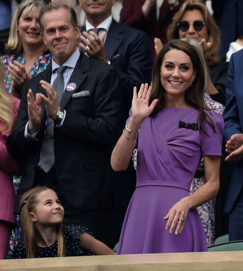 Catherine, the Princess of Wales, waves to a crowd while wearing a purple dress. Her young daughter, Princess Charlotte, smiles up at her.