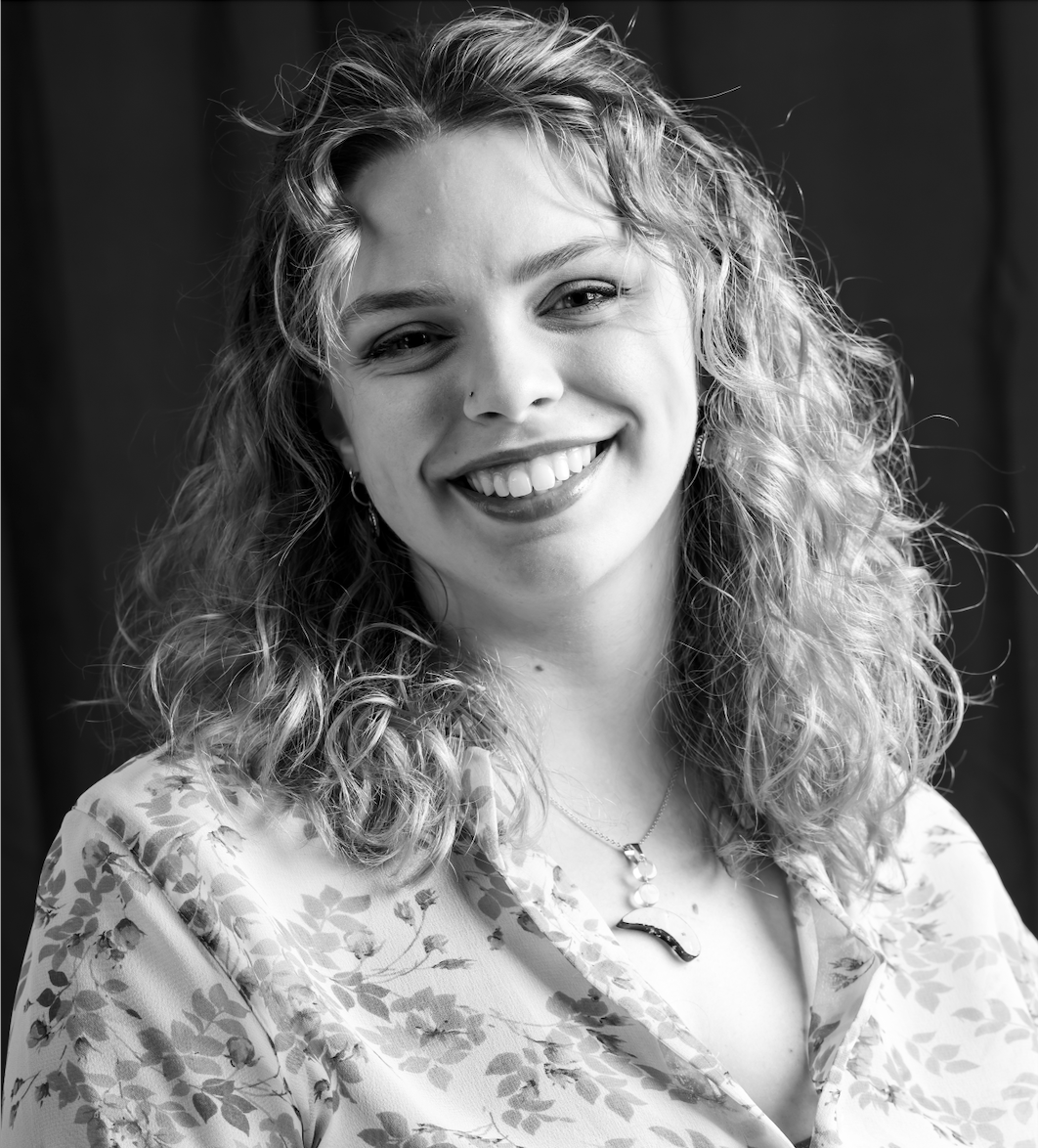 Black and white portrait of a smiling woman with curly hair, wearing a floral blouse and a necklace.