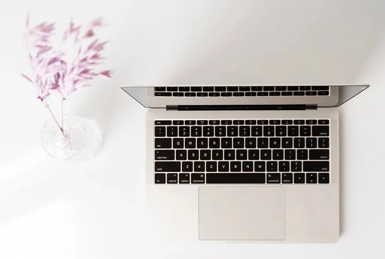 Open laptop next to a vase of purple flowers