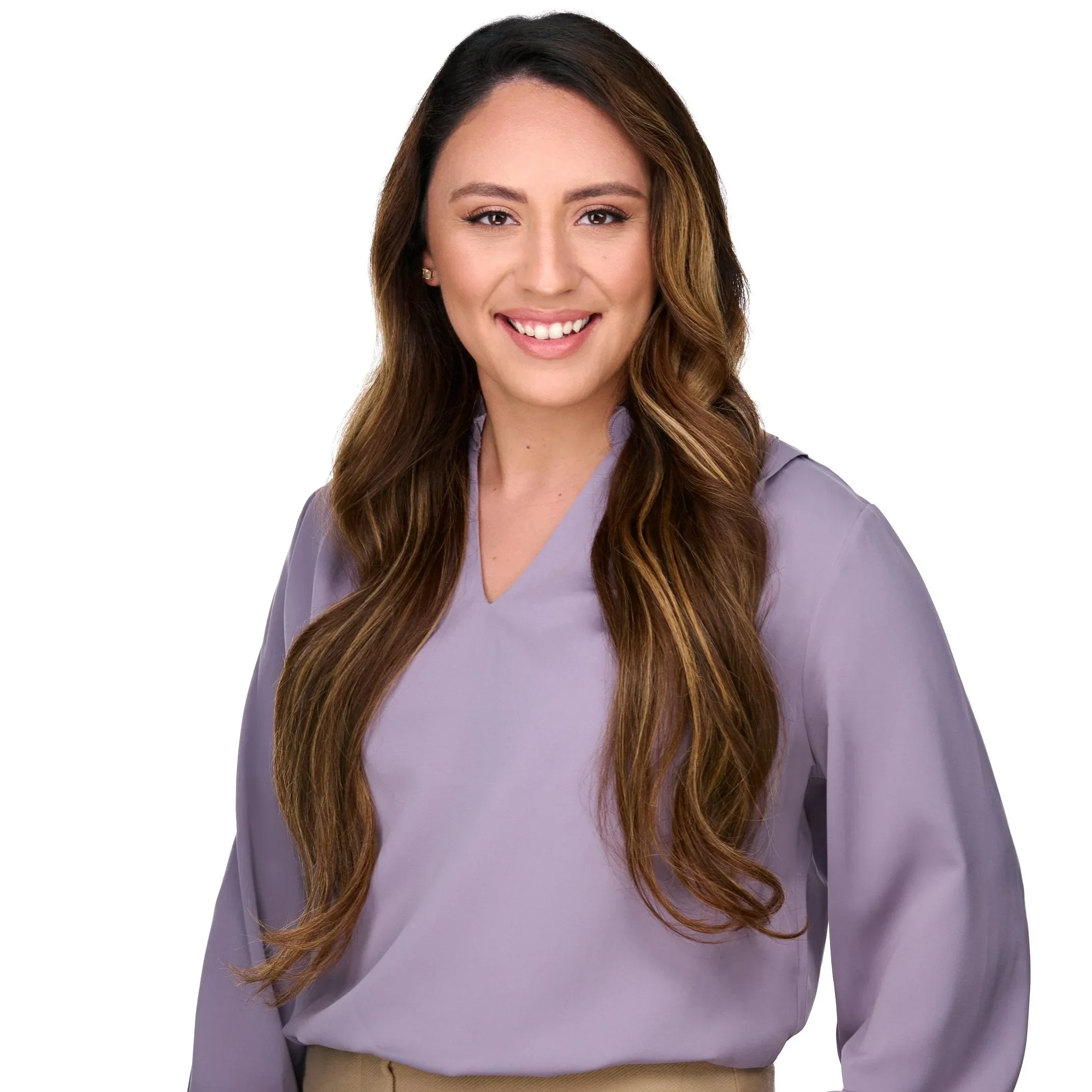 A woman with long, wavy brown hair wearing a lavender blouse, smiling, against a white background.