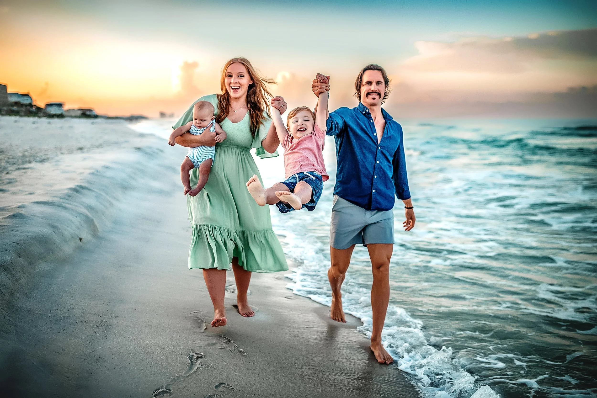 A family of four walking on the Destin beach near the emerald water swimming their little boy in the air