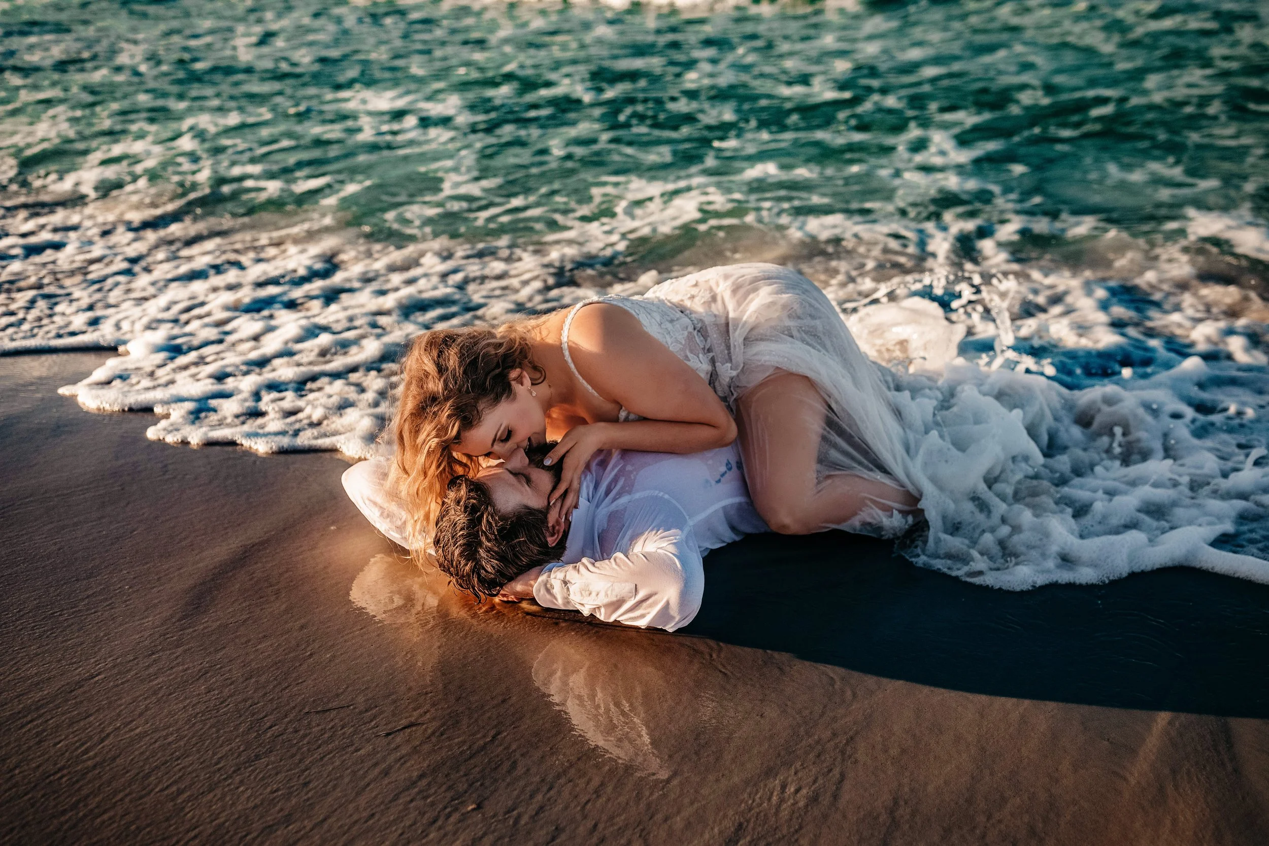 Bride and groom lying together in shoreline foam during adventurous Destin beach wedding