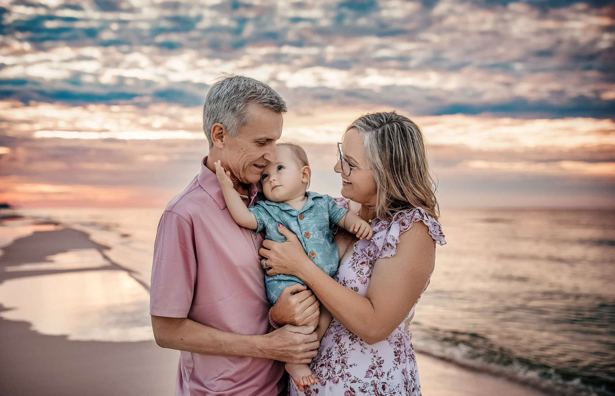 A grandma and grandpa holding their grandson while their grandson loving nestles into grandpa during their Panama City Beach Sunrise family session
