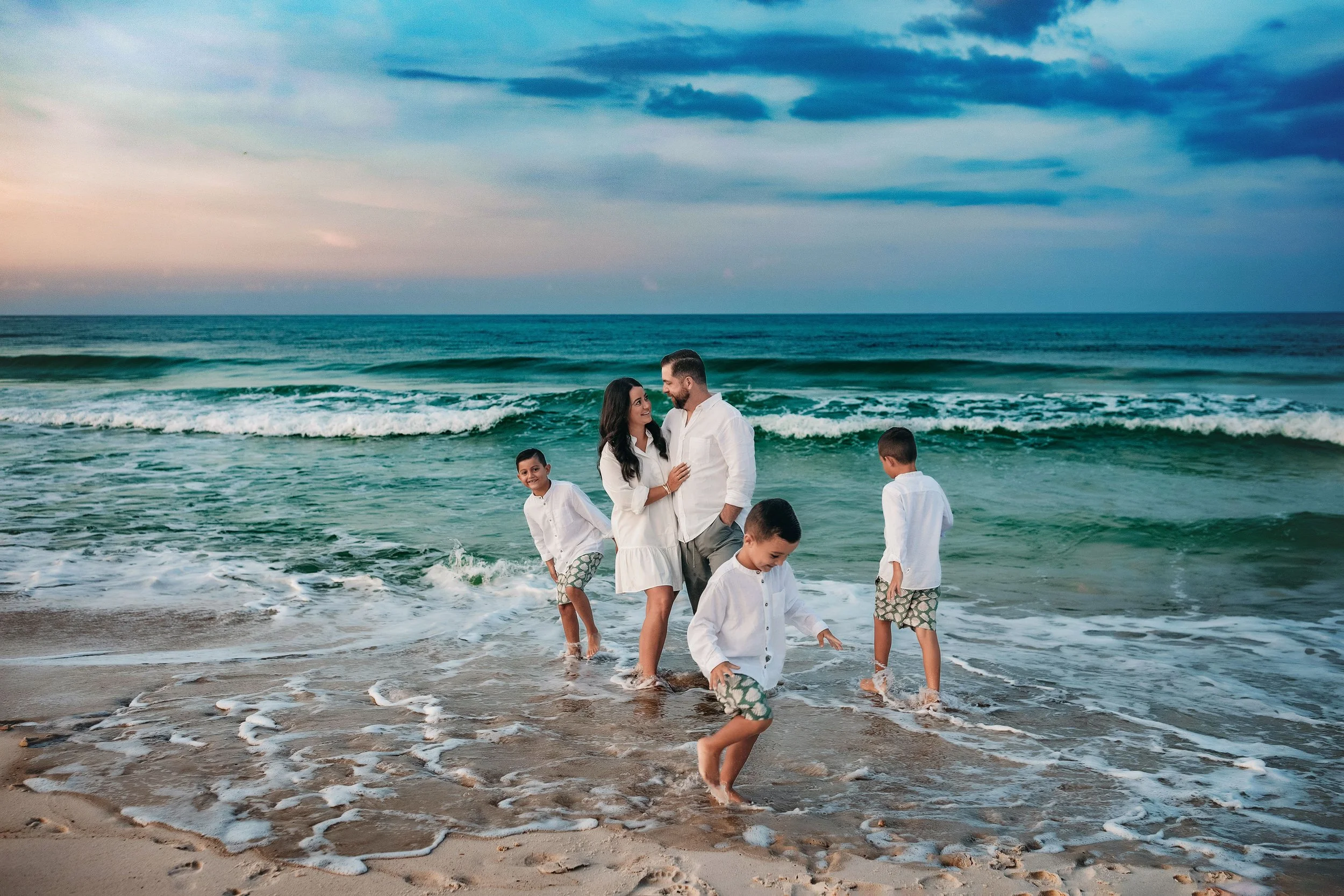 Family of three playing in waves during Santa Rosa Beach family photo session at sunset