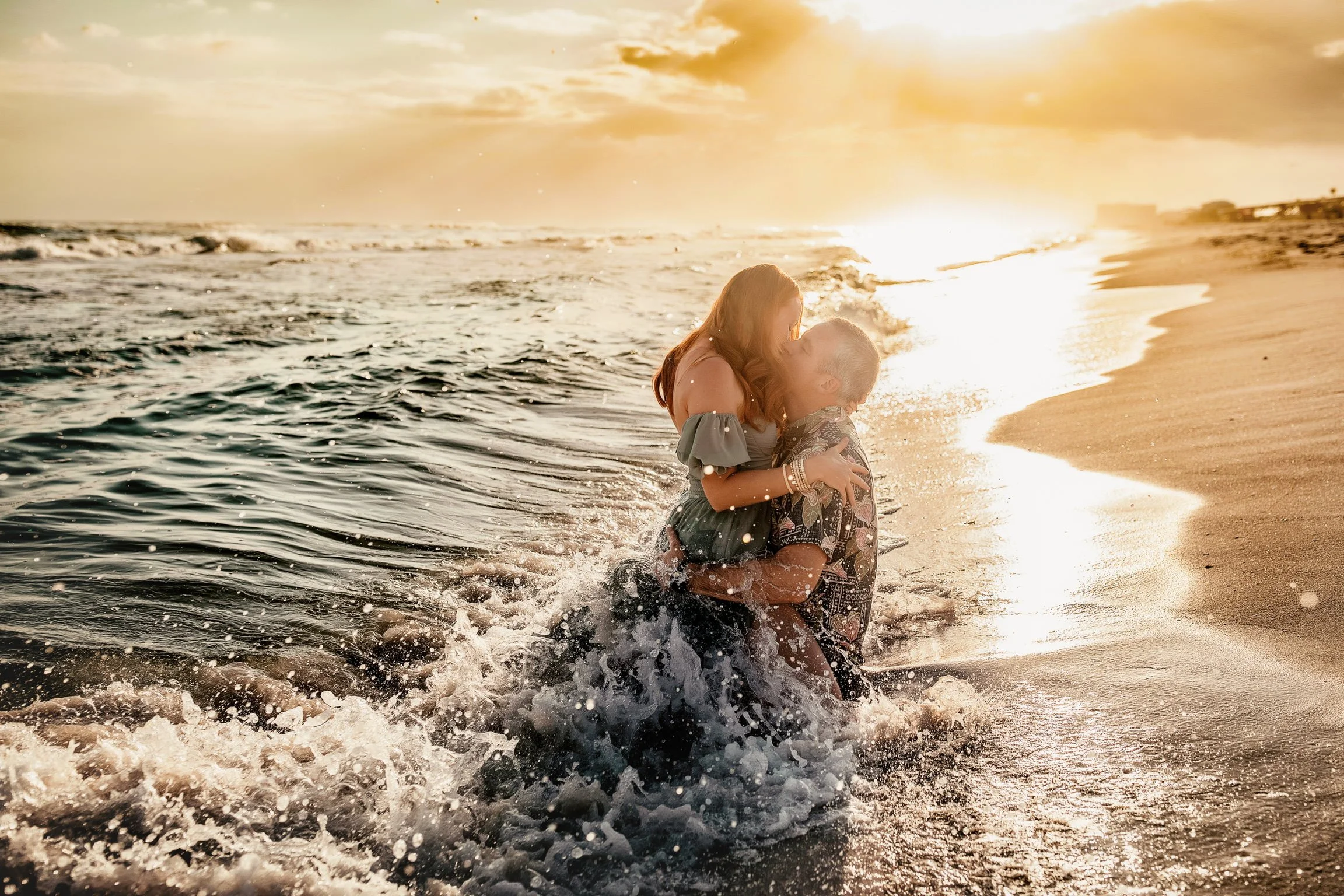 A couple in the waves at sunset during their sunset couples session on the Miramar beach