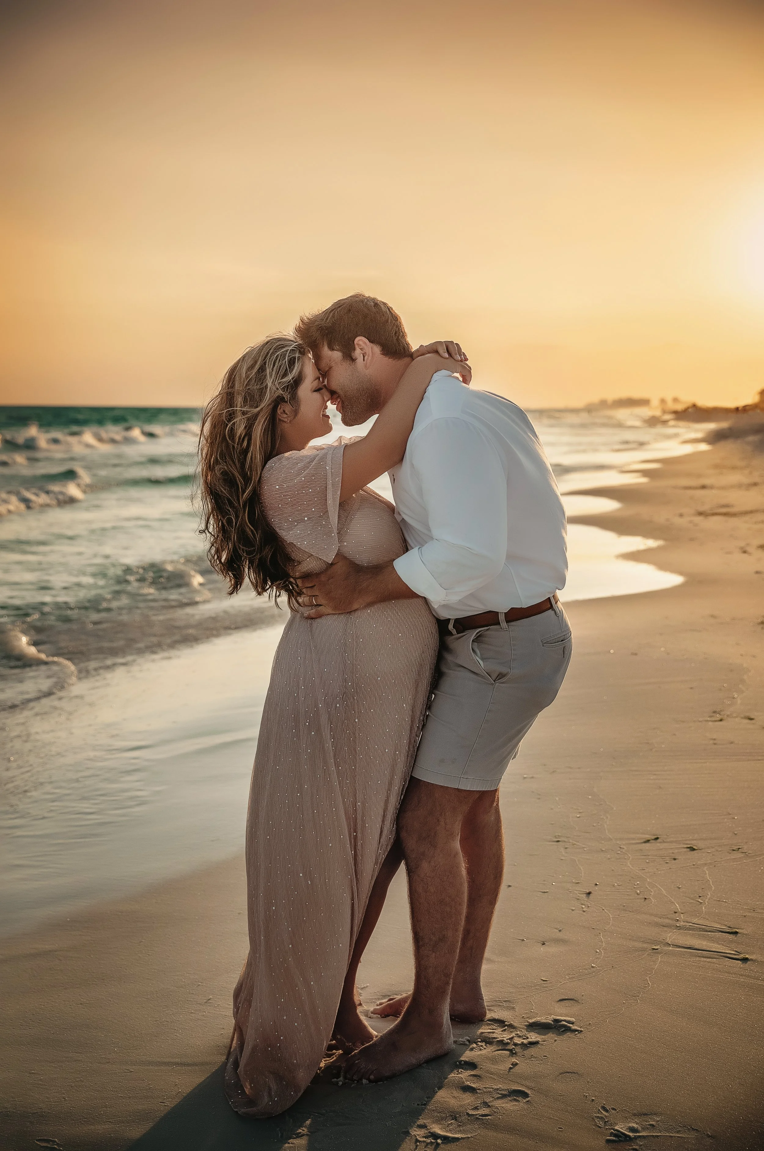 A luxury maternity photography session in Seaside, FL, featuring a couple embracing on the beach with an editorial, romantic feel.