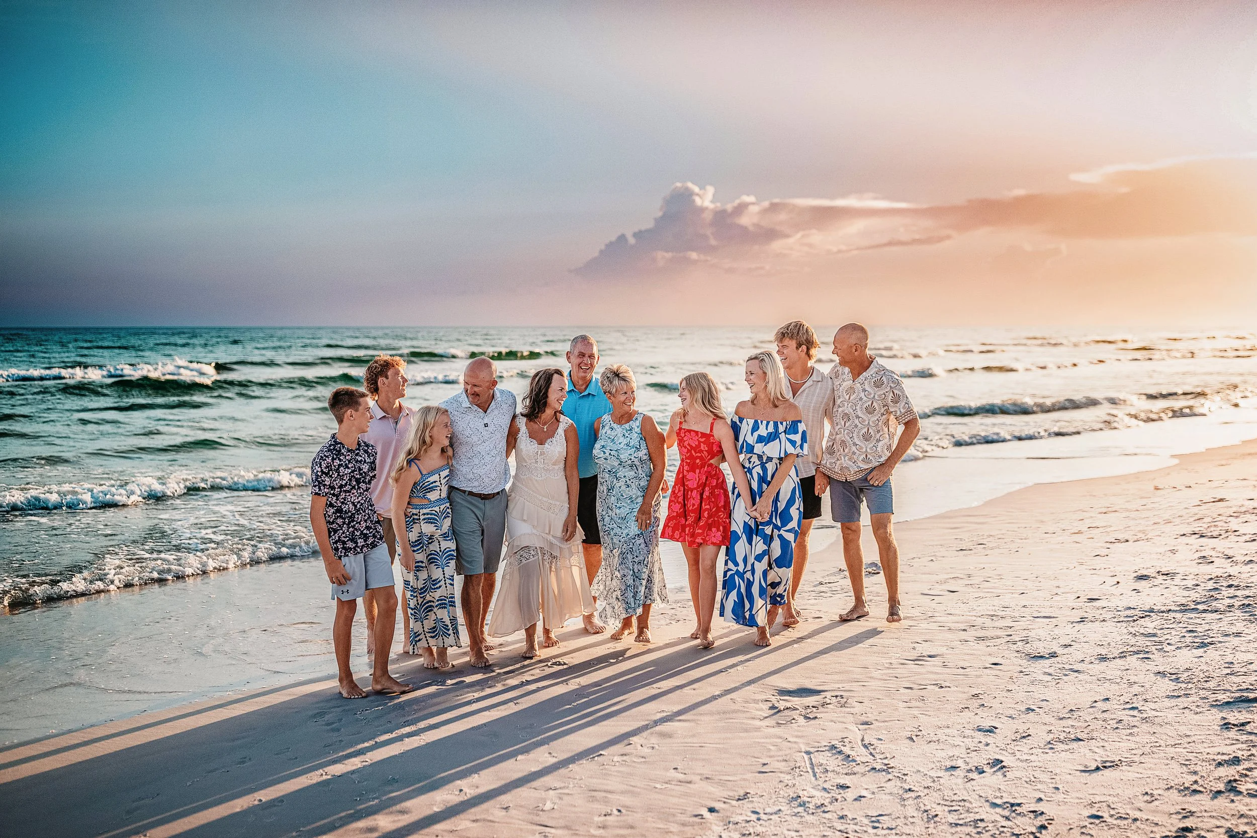 Extended family walking together barefoot along the shoreline during a 30A beach photography session, laughing as golden sunset light reflects across the wet sand.