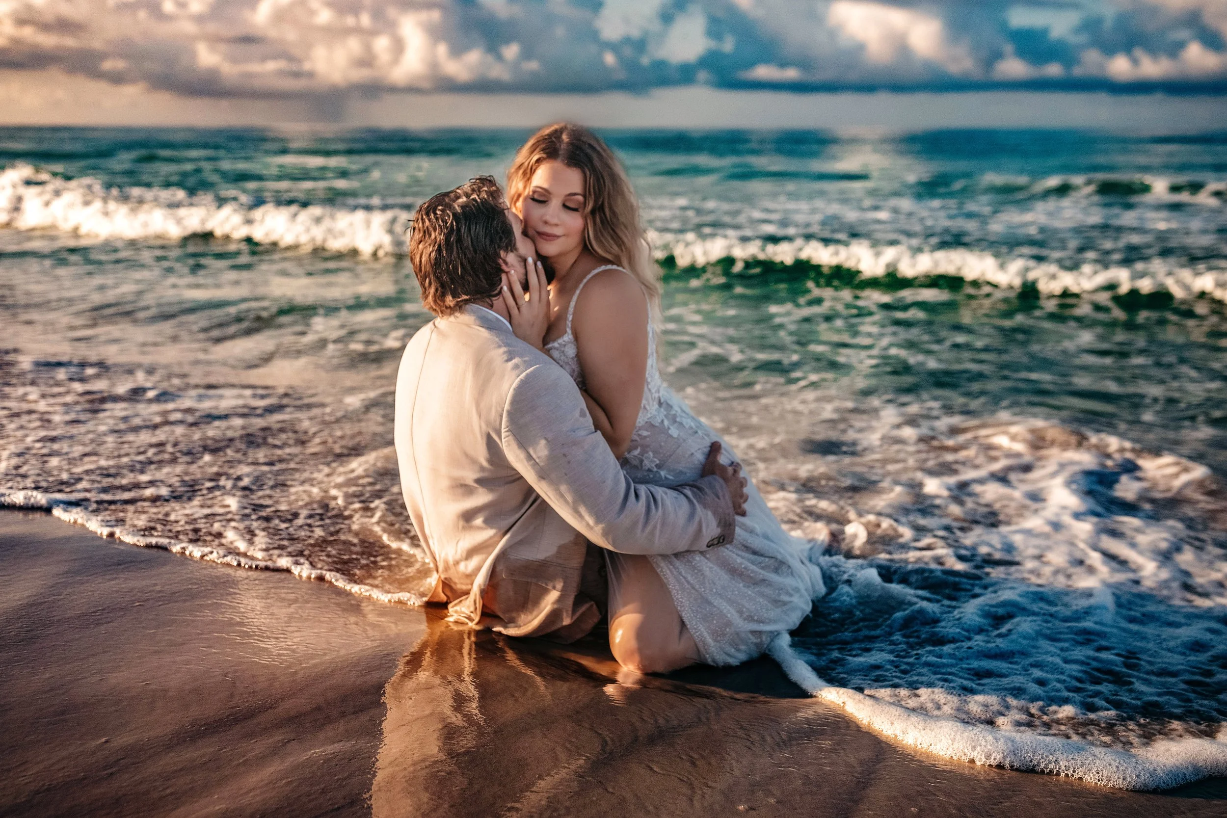 Bride and groom embracing in the shoreline waves during sunrise beach wedding