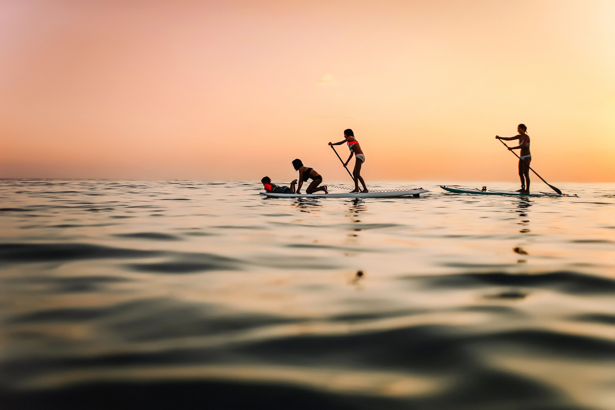 Four people, including children, paddleboarding on calm water during sunset.