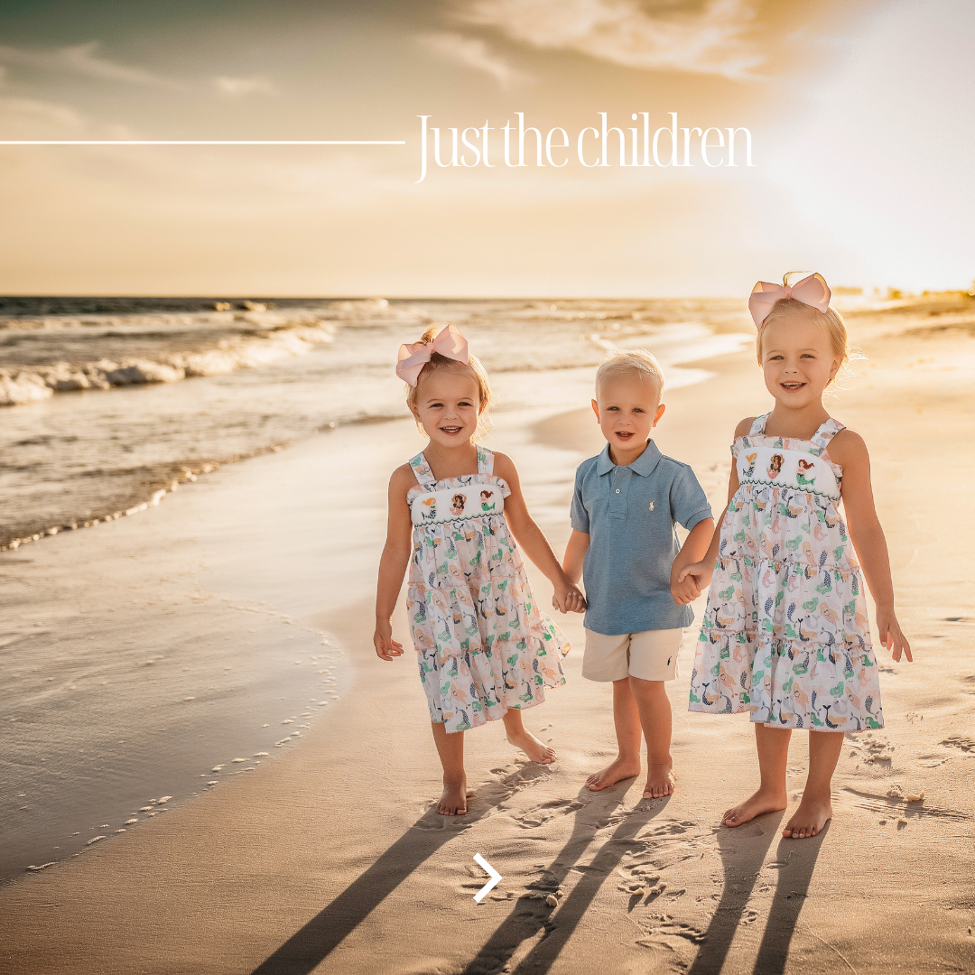Three young grandchildren in matching mermaid dresses and pink bows walking hand in hand on the 30A beach at golden hour sunset, just the children photos by 30A beach photographer Lisa Marie