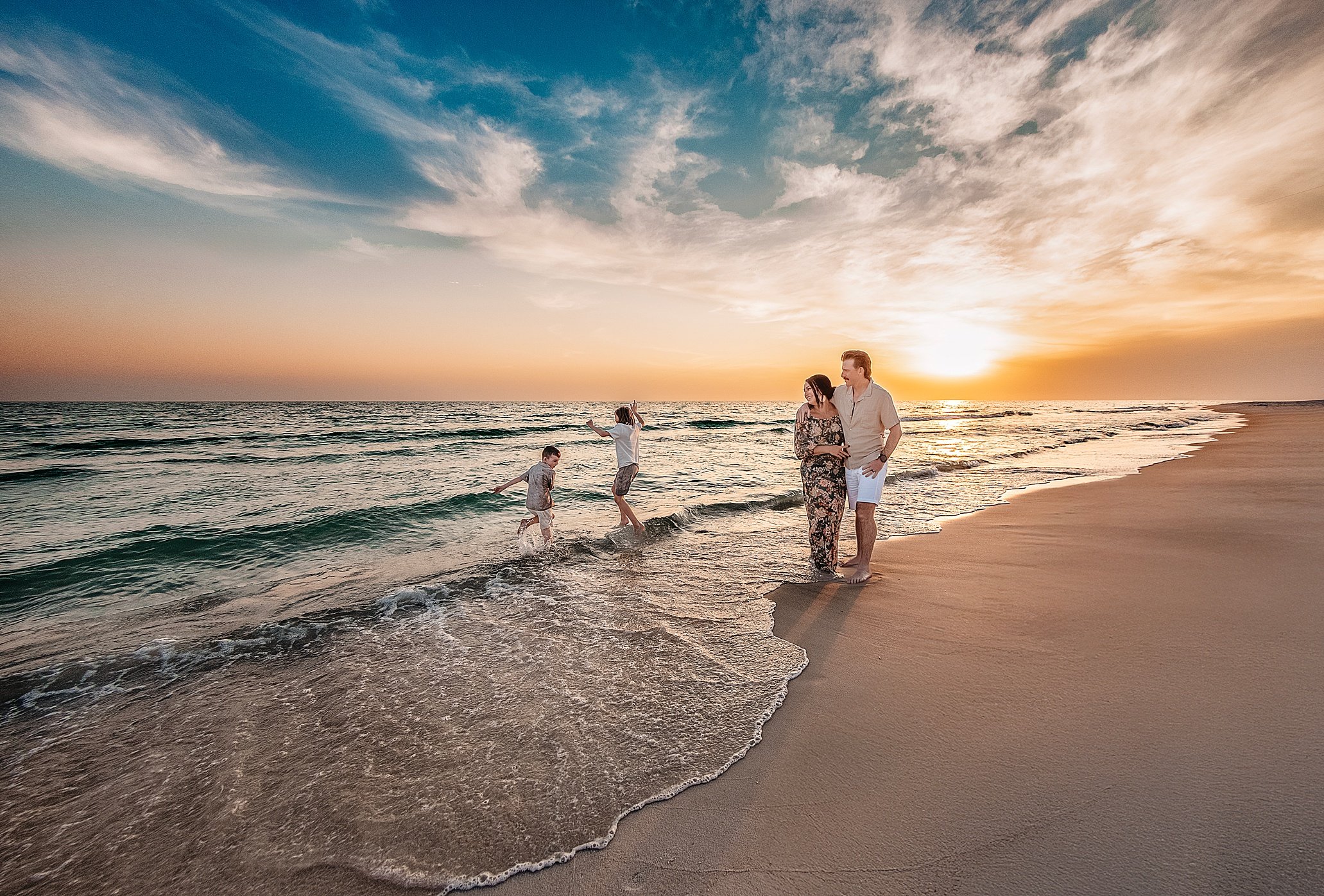 A mother and father standing on the shoreline watching their two boys splash in the water during their 30A Sunset Beach Session in Rosemary Beach with 30A Beach Photographer, Lisa Marie