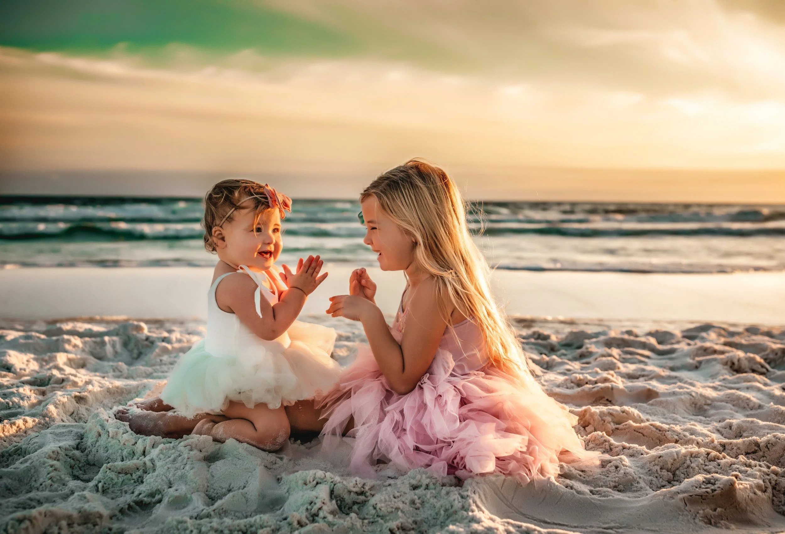 Two sisters sitting in the sand and playing together during a sunset family photo session on 30A
