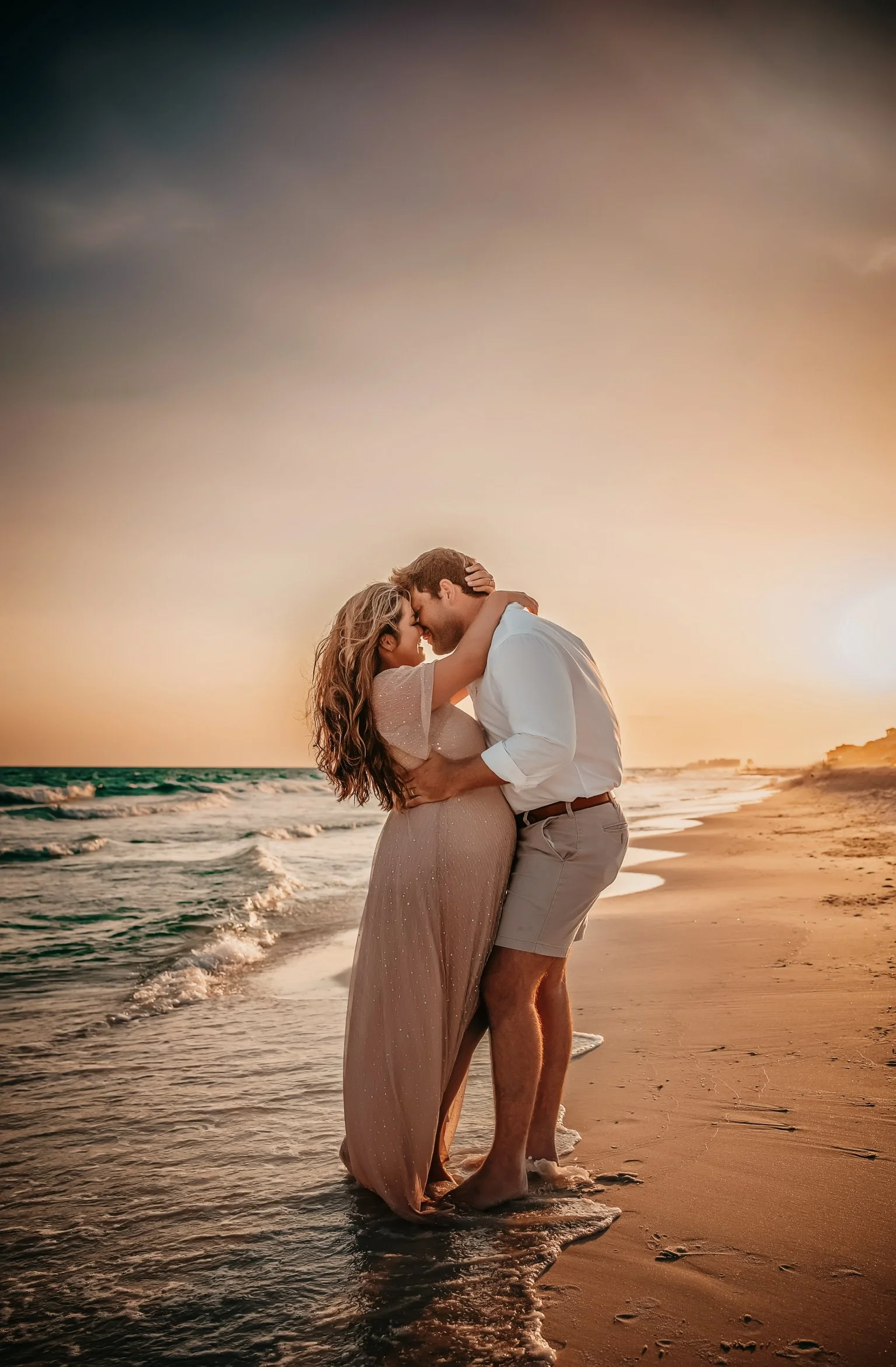 Expectant mother and father embracing near the emerald water in Destin Florida during their sunset maternity session