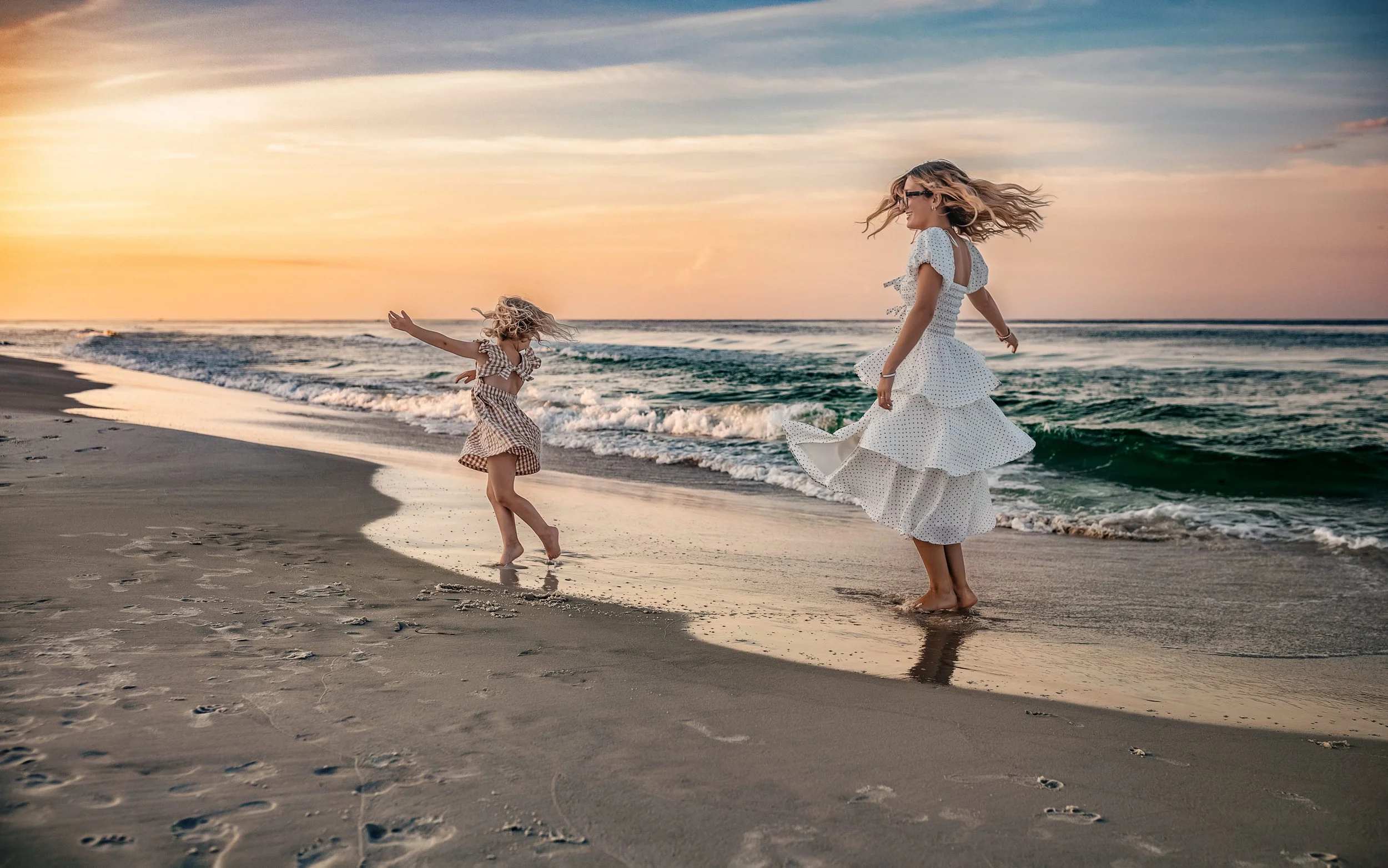 sisters twirling near the emerald water in Destin during their sunrise family beach session