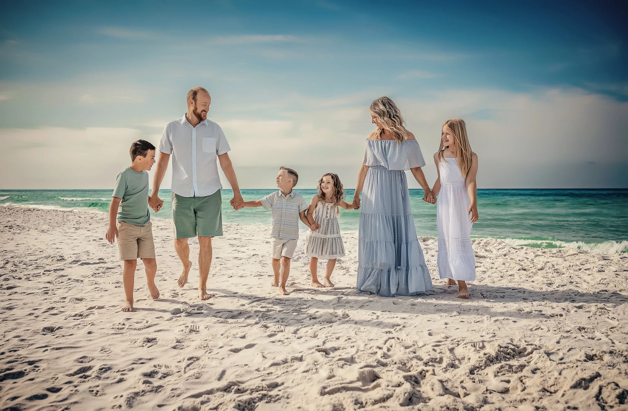 Family of six walking hand in hand on Seaside Florida beach — mom in blue maxi, coordinated green and white tones — 30A family beach photographer