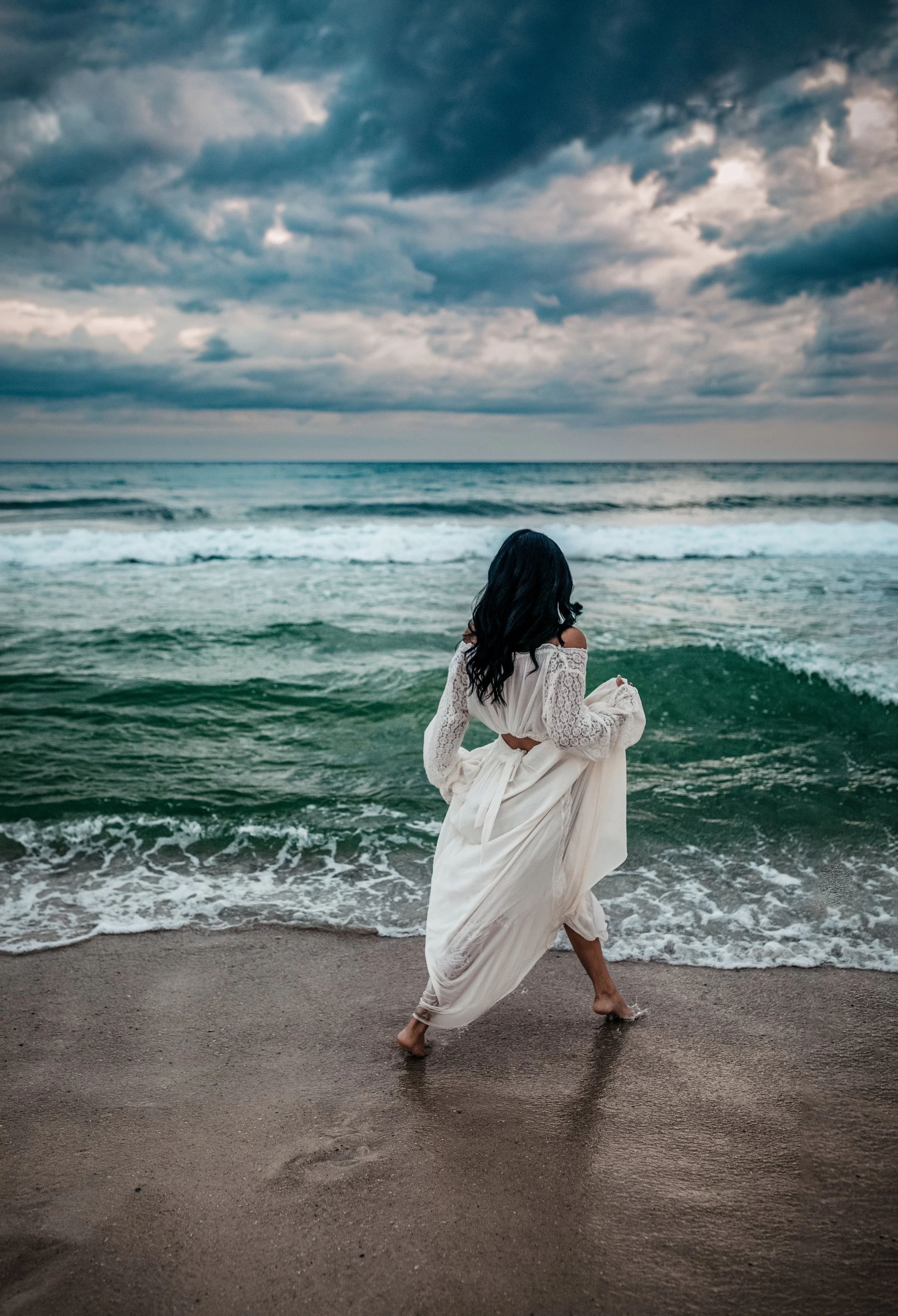 A high school senior girl walking towards the Gulf of Mexico water at sunset during her senior beach session.