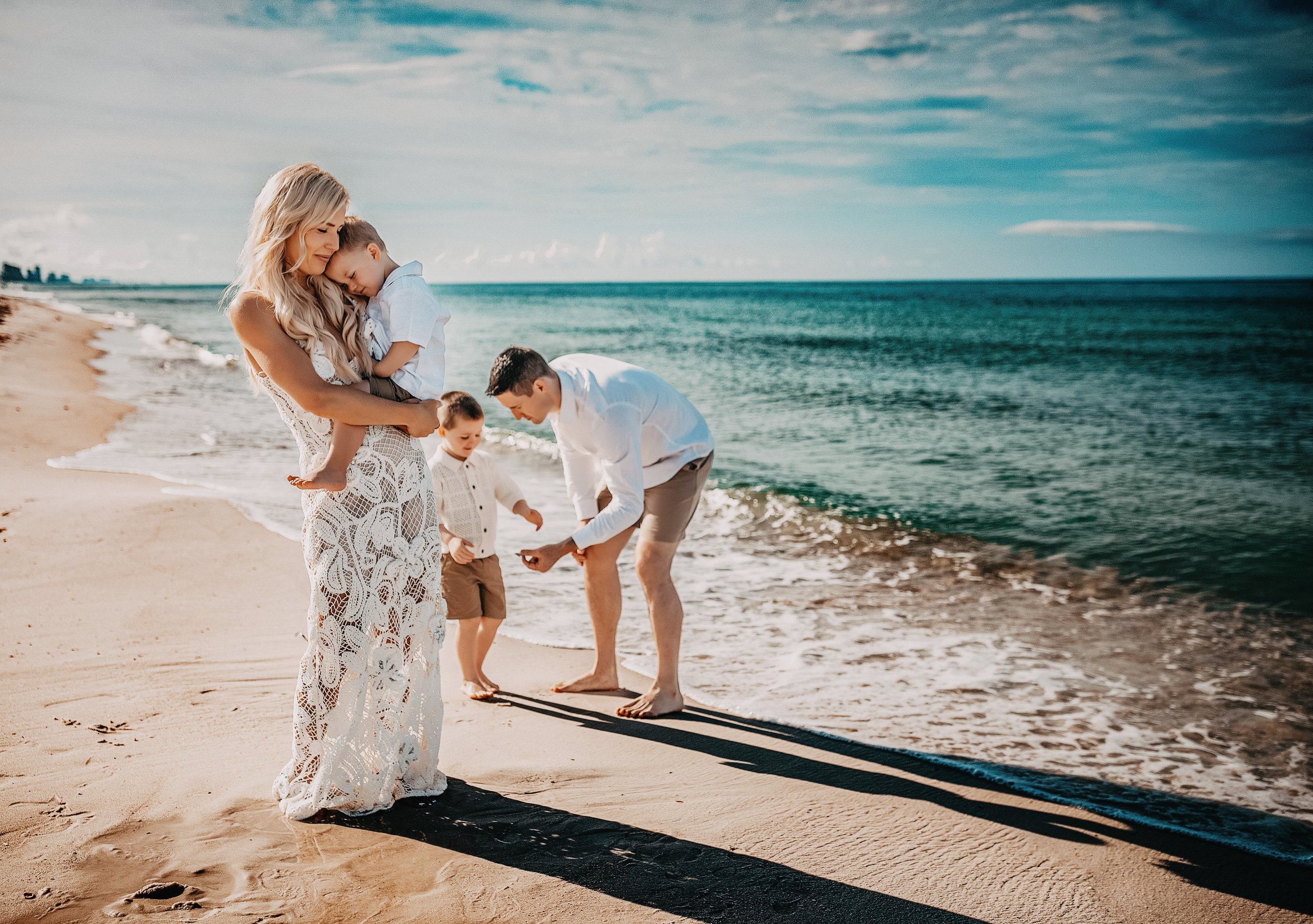 A family of four enjoying a day at the beach, with the mother holding a child, and the father and two kids playing near the shoreline.