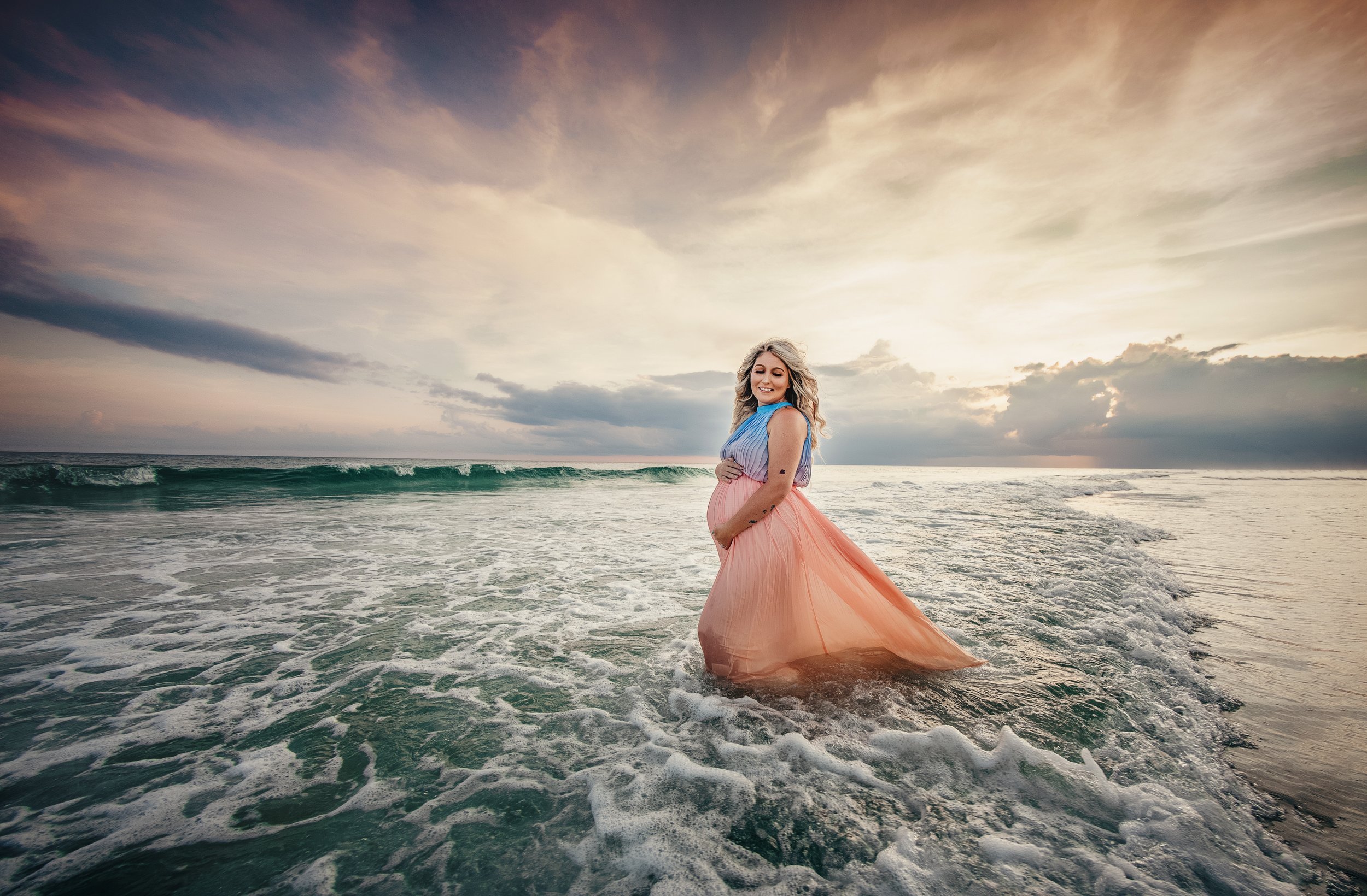 Expectant mother holding her belly while standing in the emerald water during her 30A maternity session.