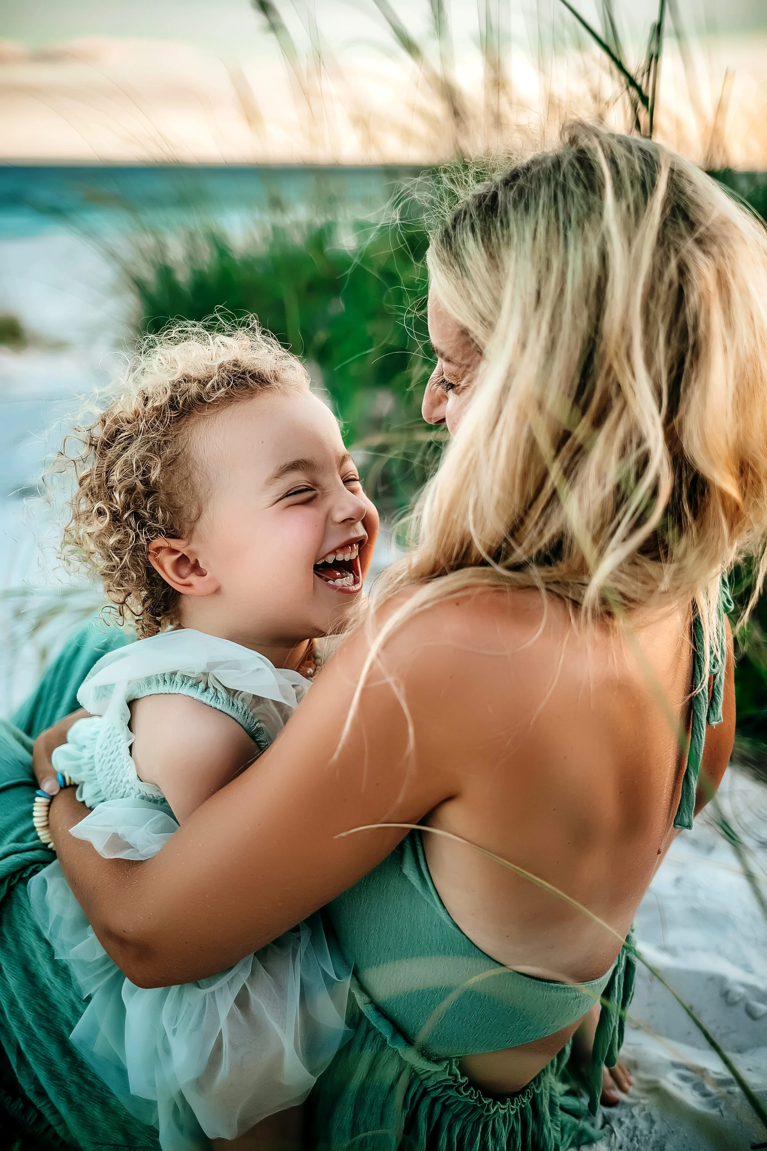 A mother and daughter laughing and embracing during their sunset family beach session in seaside,fl
