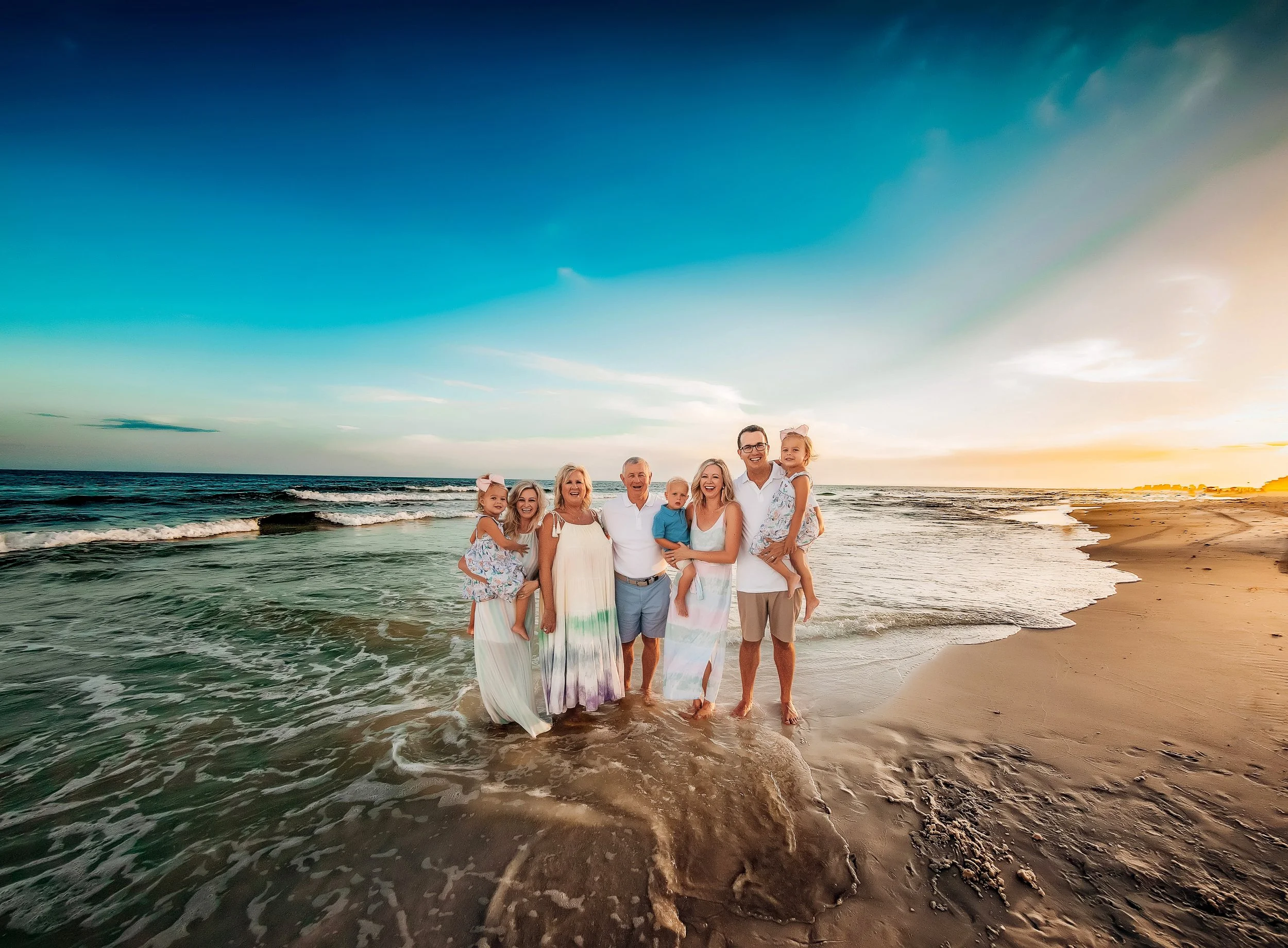 Extended family 30A beach of eight standing in the water laughing at the camera during their sunset beach family session