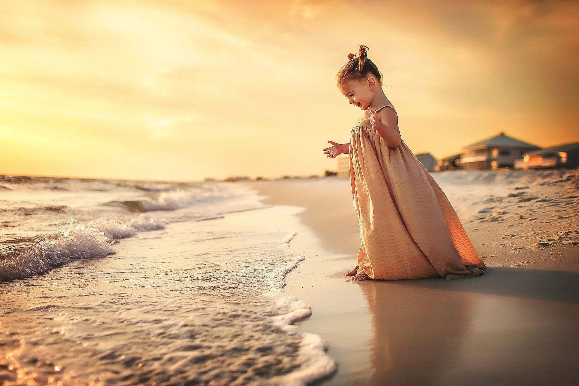 Little girl in a golden dress walking toward the waves.