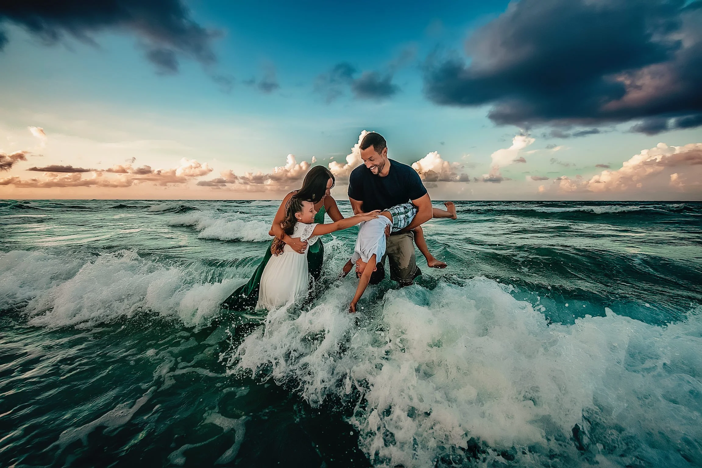 A family of four in the emerald water off the Miramar beach during their sunrise session
